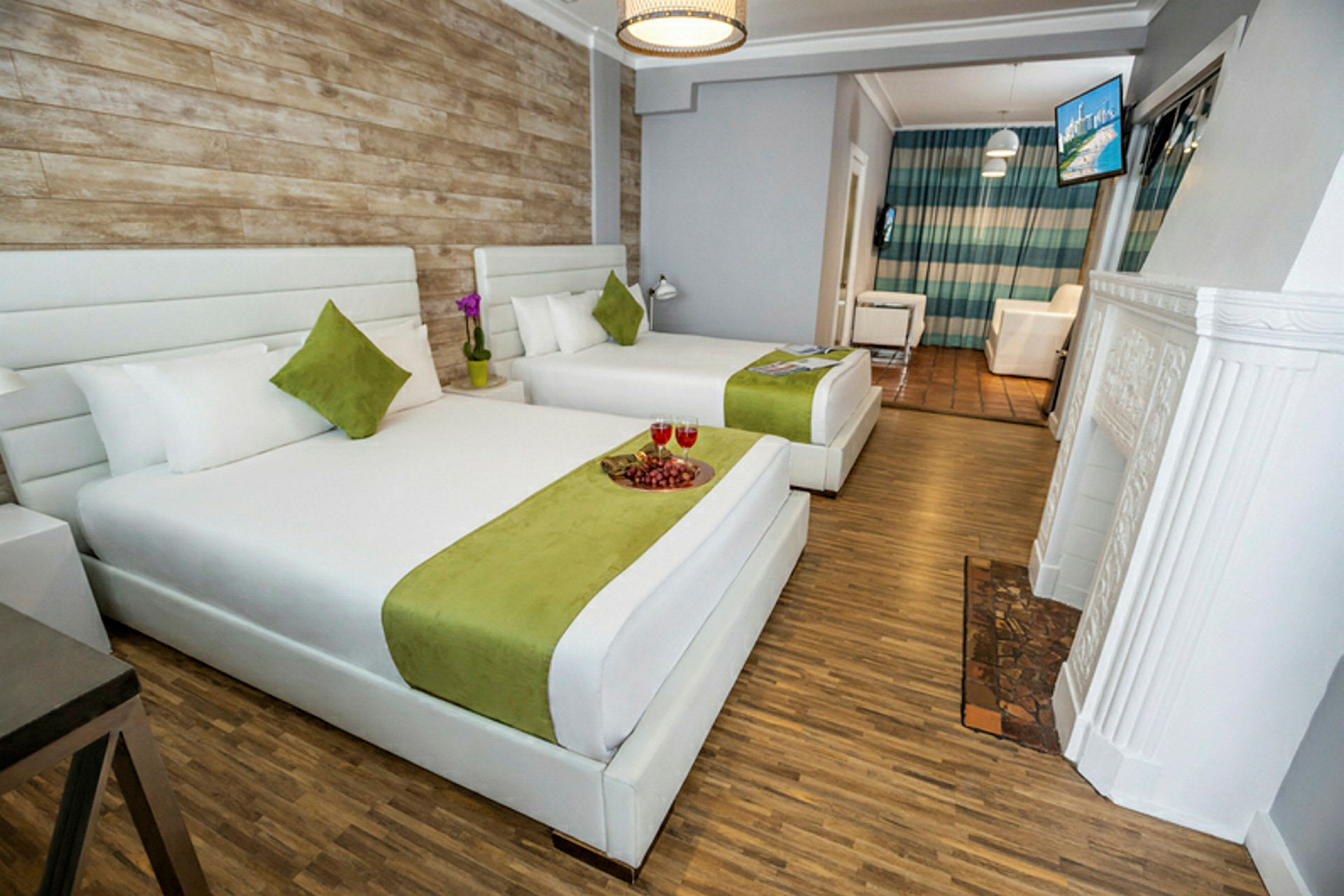 Hotellihuone, jossa on kaksi suurta sänkyä, valkoiset ja vihreät vuodevaatteet, puulattia ja rustiikkityylinen seinä. (Tekoälyn luoma teksti)