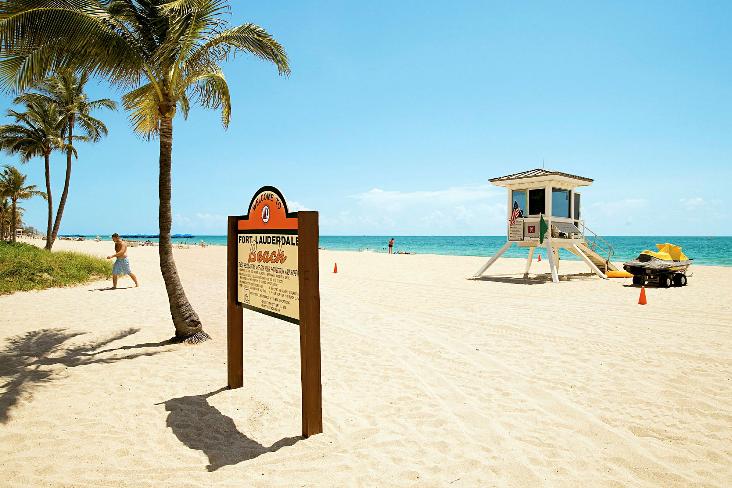 Hiekkaranta, jossa on palmuja, kyltti, joka toivottaa tervetulleeksi Fort Lauderdale Beachille, ja pelastustorni. (Tekoälyn luoma teksti)