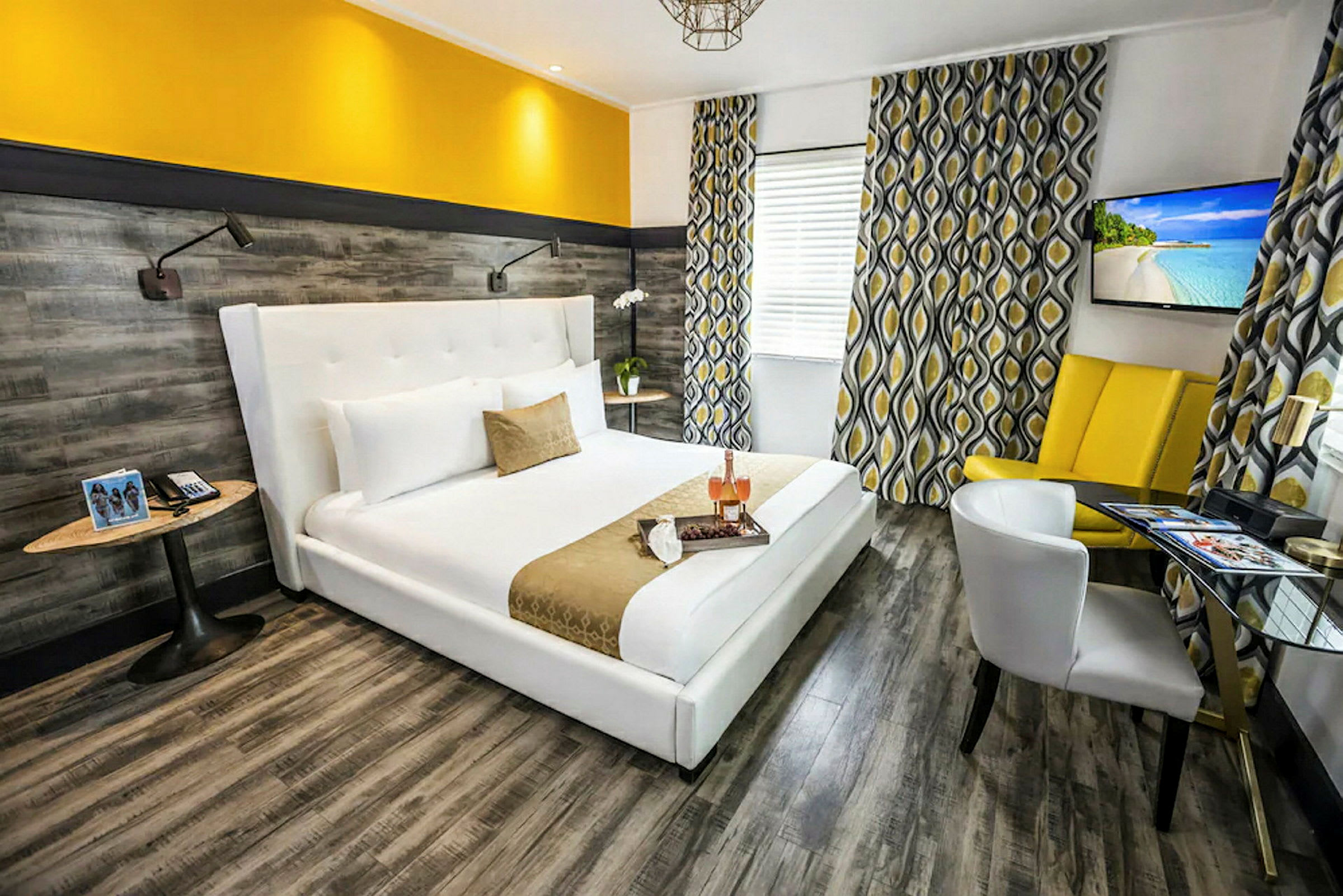 Moderni hotellihuone, jossa on leveä valkoinen sänky ja keltaisia yksityiskohtia sisustuksessa. Seinissä on puukuosinen pinta ja ikkunoita koristavat kuvioidut verhot. (Tekoälyn luoma teksti)