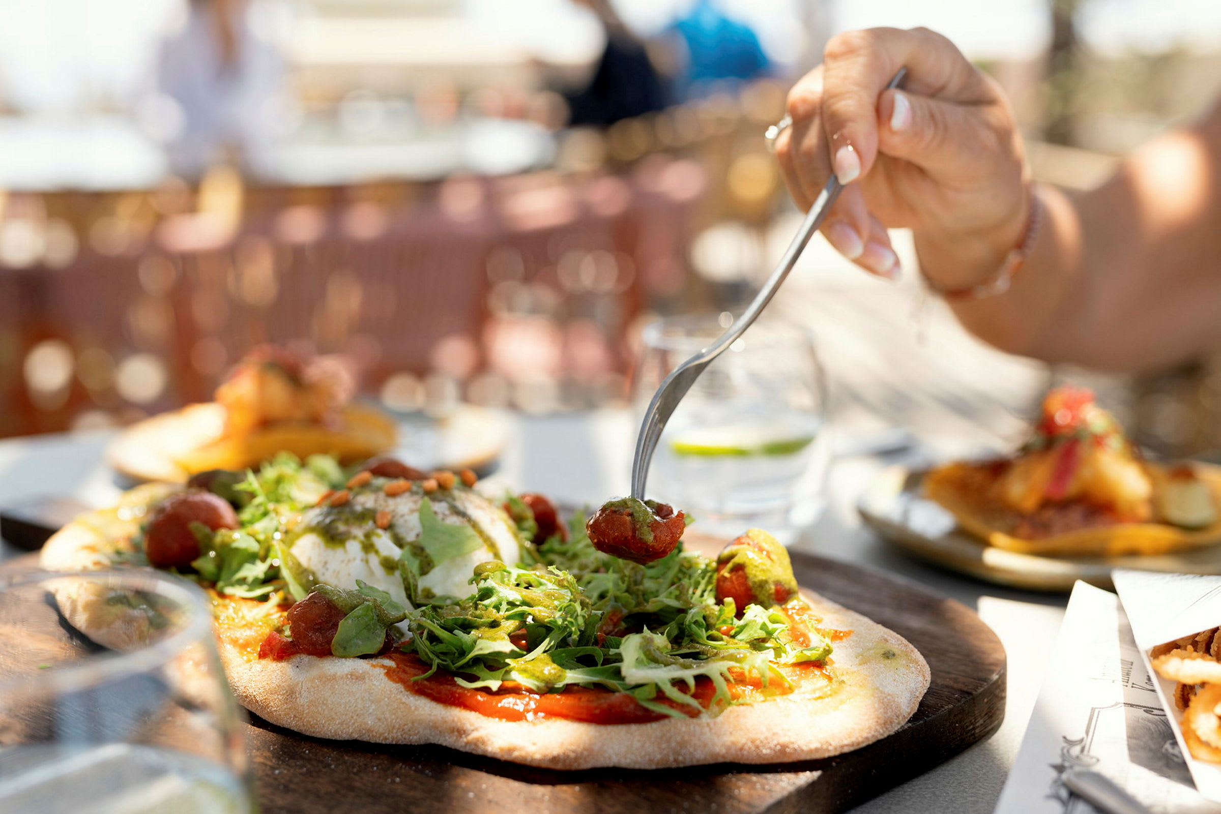 Käsi käyttää haarukkaa ottamalla ruokaa pizzasta, jonka päällä on salaattia ja lisukkeita. (Tekoälyn luoma teksti)