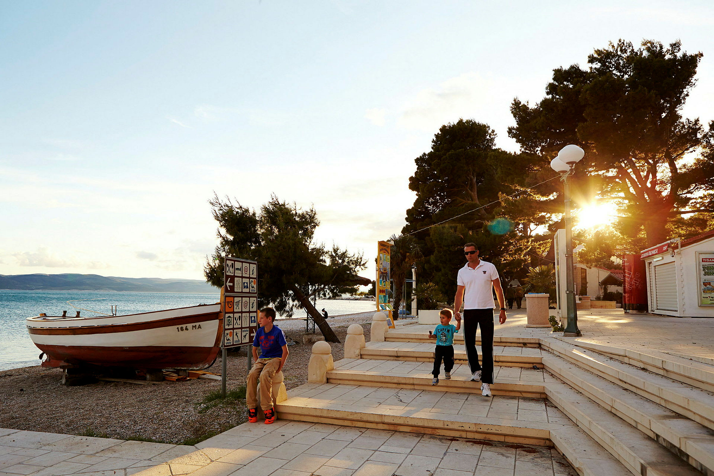 Rantakävelytie, vene, puita ja ilta-aurinko. (Tekoälyn luoma teksti)