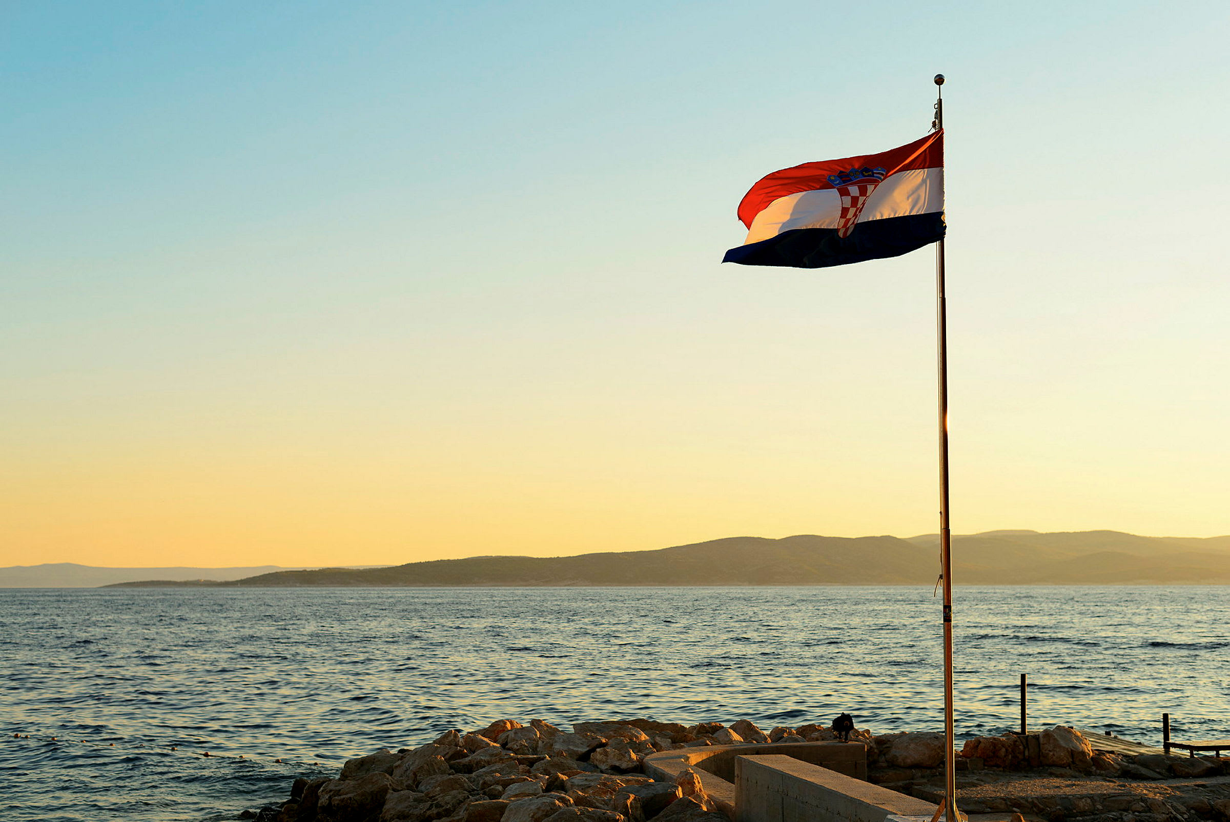 Kroatian lippu liehuu rannikolla auringonlaskun aikaan. (Tekoälyn luoma teksti)
