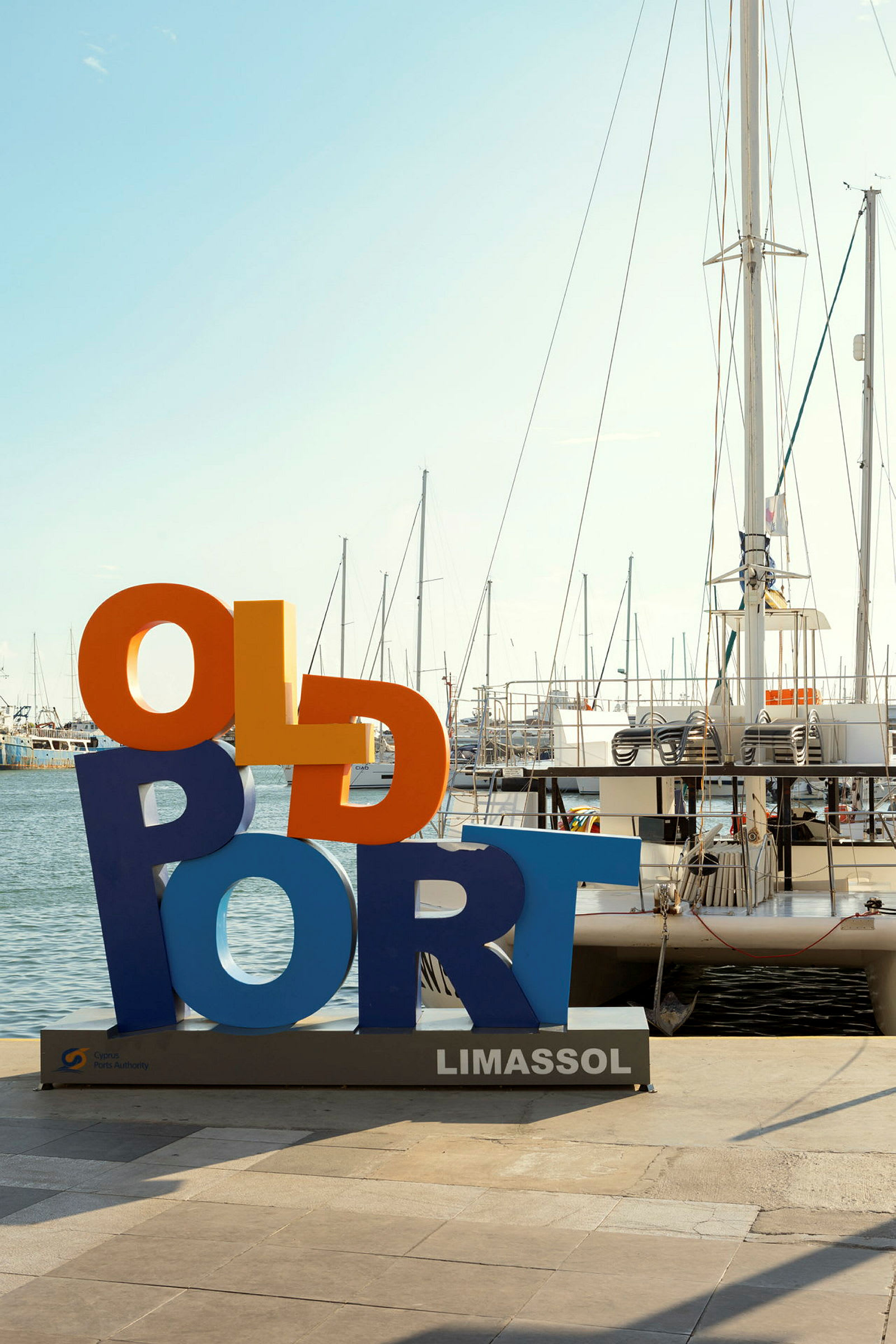 Värikäs kyltti, jossa lukee 'Old Port', Limassolin satamassa, taustalla purjeveneitä. (Tekoälyn luoma teksti)