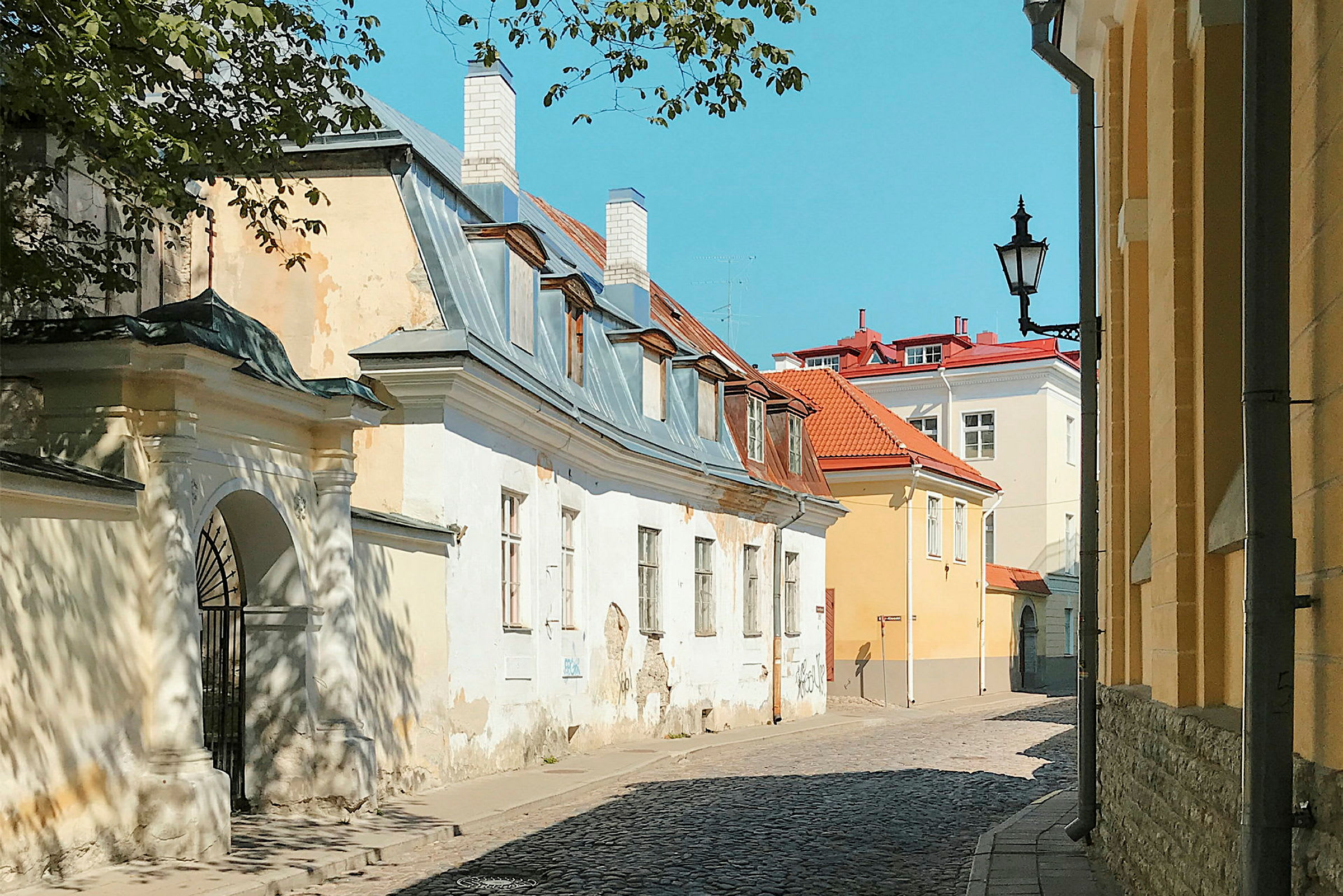 Kapea katu, jota reunustavat vanhat rakennukset tiili- ja peltikatoilla kirkkaan sinisen taivaan alla. (Tekoälyn luoma teksti)