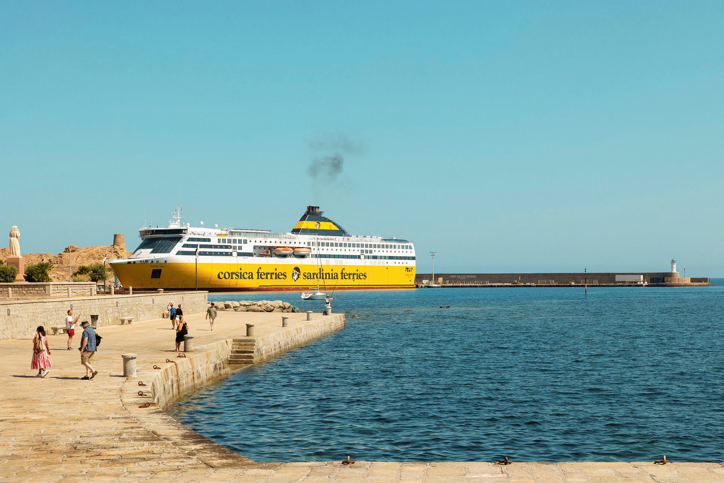 Kelta-valkoinen Corsica Ferries -lautta on laiturissa, ja ihmisiä kävelee laiturialueella meren näkyessä etualalla. (Tekoälyn luoma teksti)