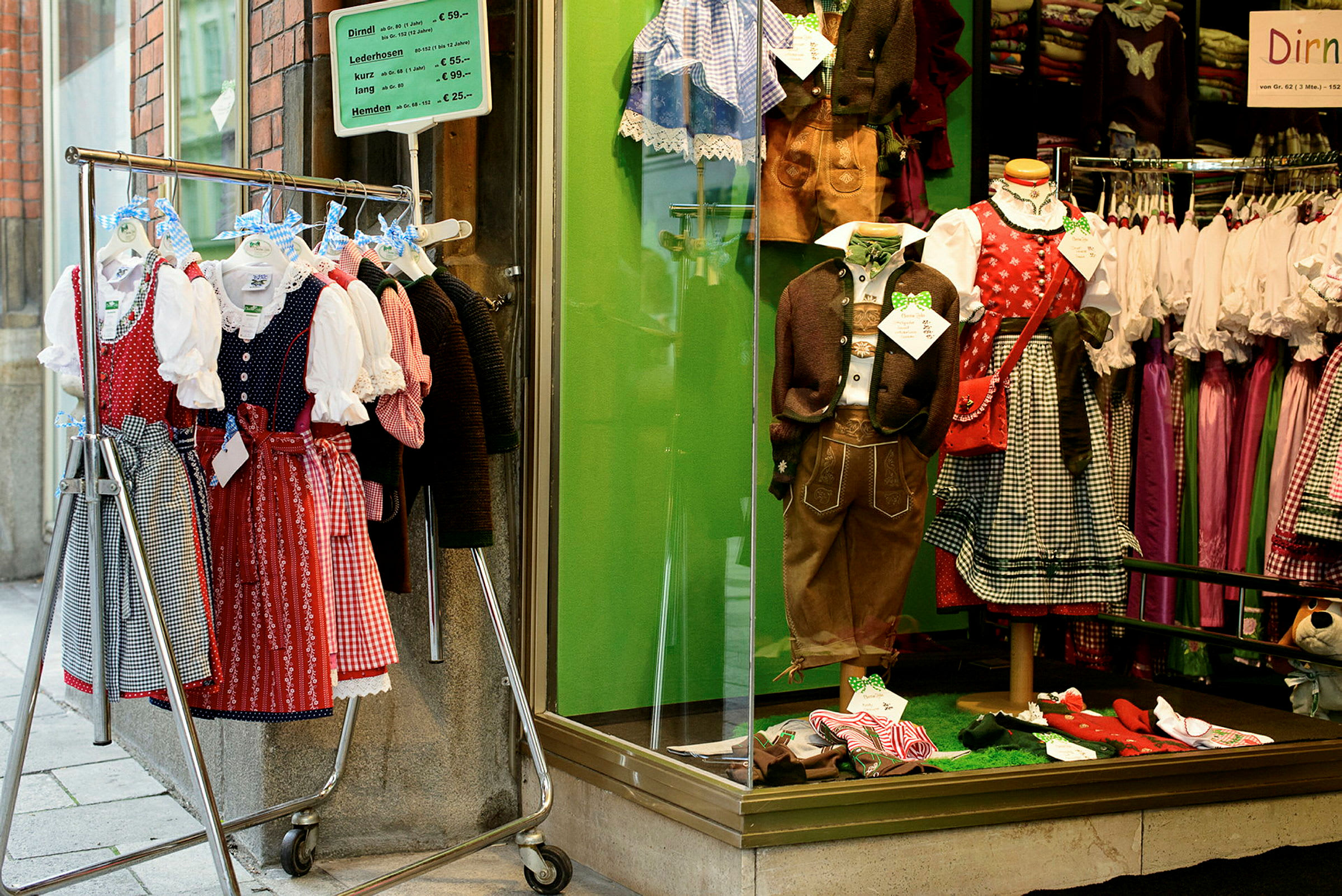 Näyteikkuna perinteisine kansallispukuineen sekä ulkopuolella vaaterekki täynnä dirndl-mekkoja. (Tekoälyn luoma teksti)