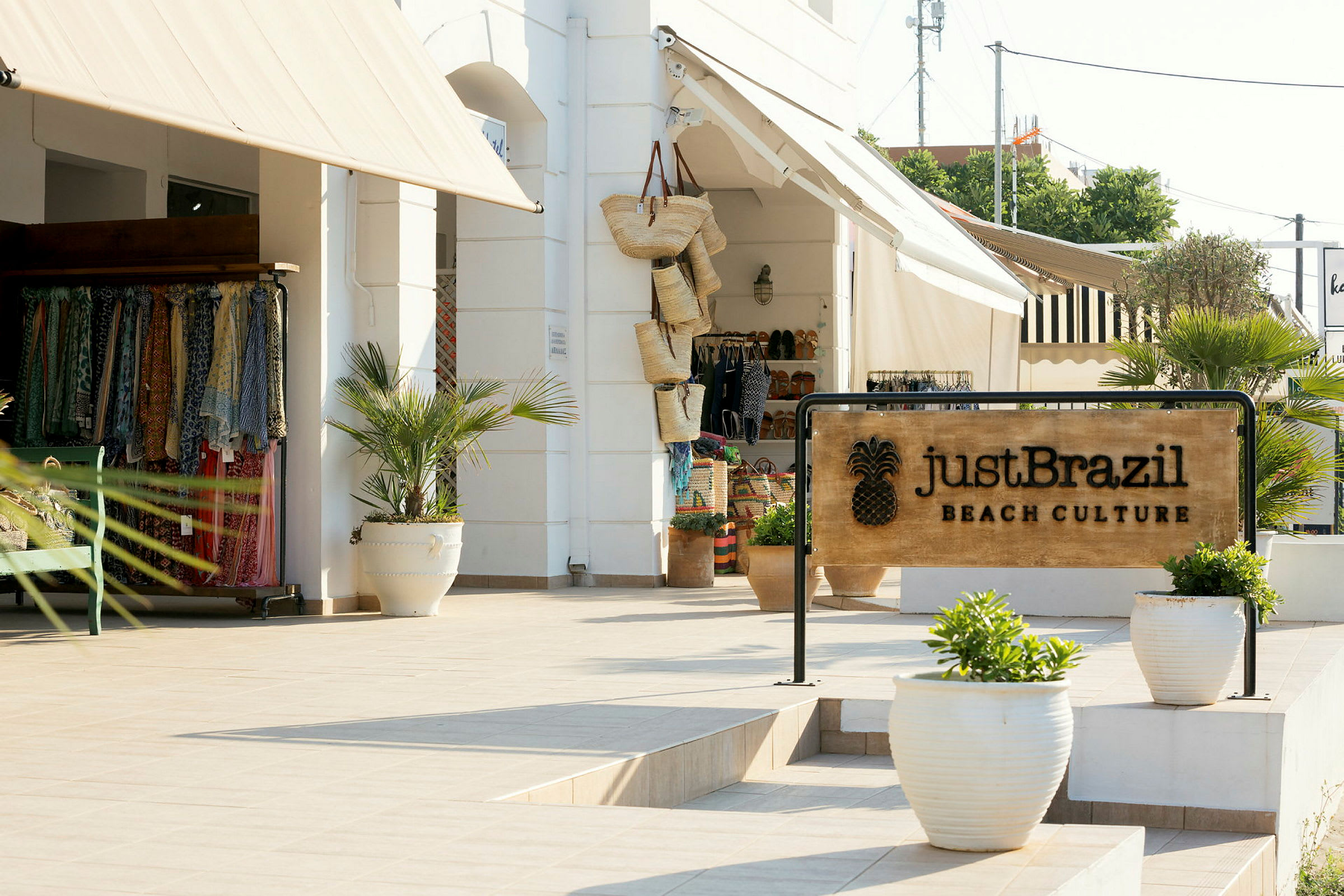 Kyltti, jossa lukee 'Just Brazil Beach Culture', myymälän edessä, jossa on puuvillavaatteita ja koreja. (Tekoälyn luoma teksti)