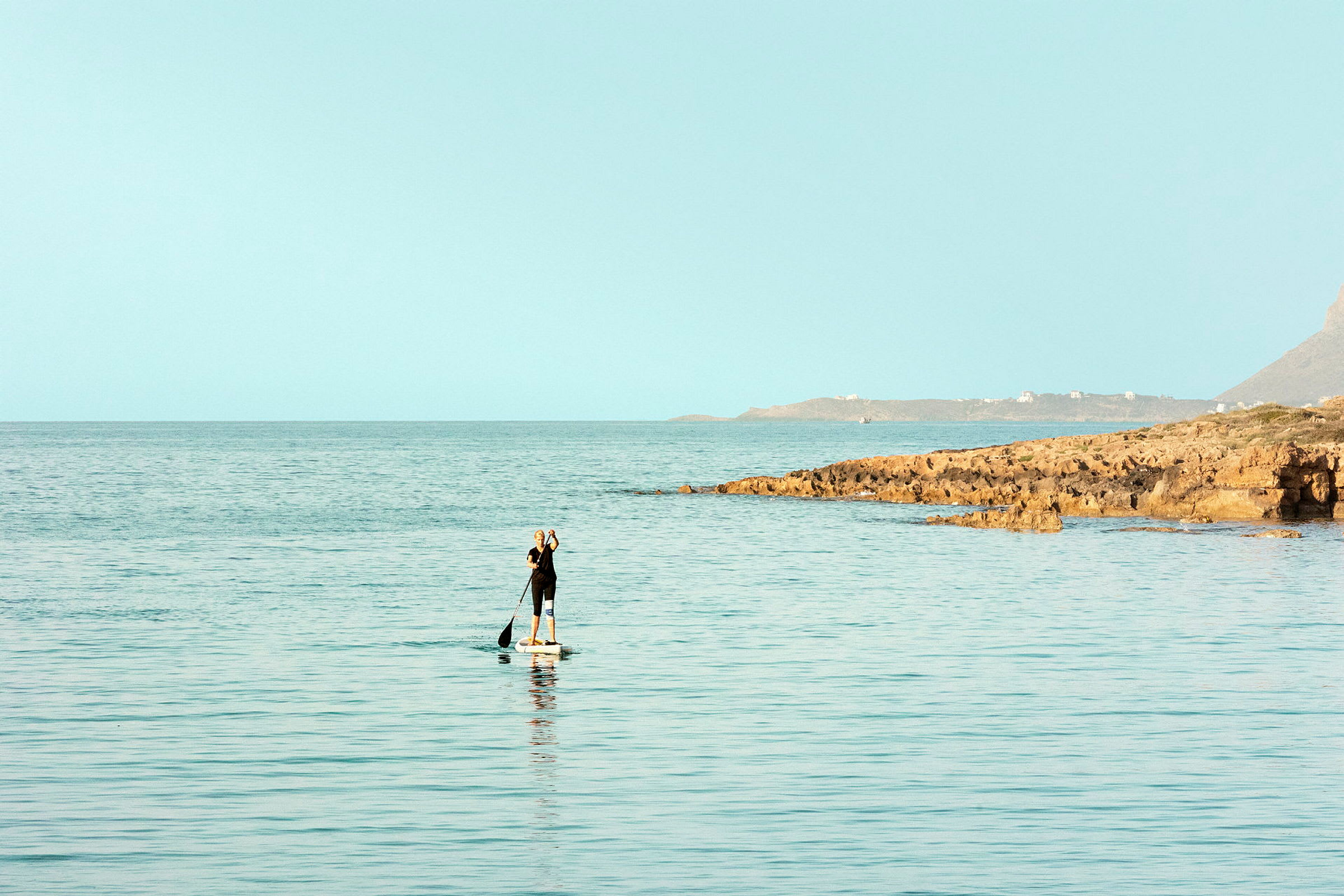 Henkilö meloo paddleboardilla meressä lähellä kivistä rantaa. (Tekoälyn luoma teksti)