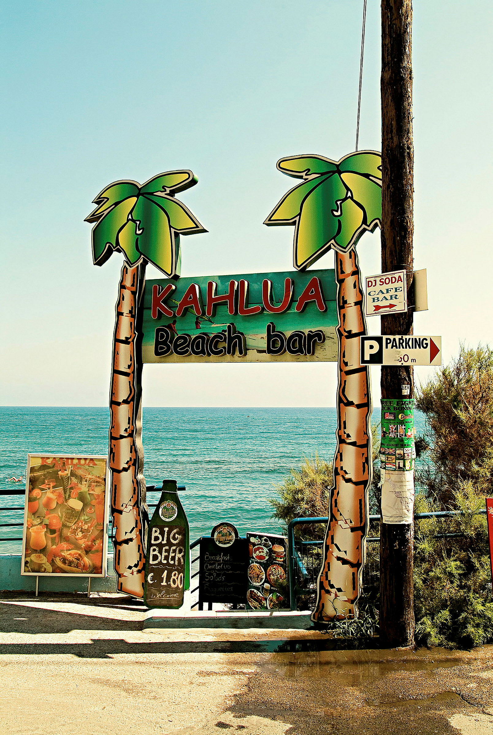 Kuva, jossa kyltti tekstillä 'Kahlua Beach Bar' meren edessä. (Tekoälyn luoma teksti)