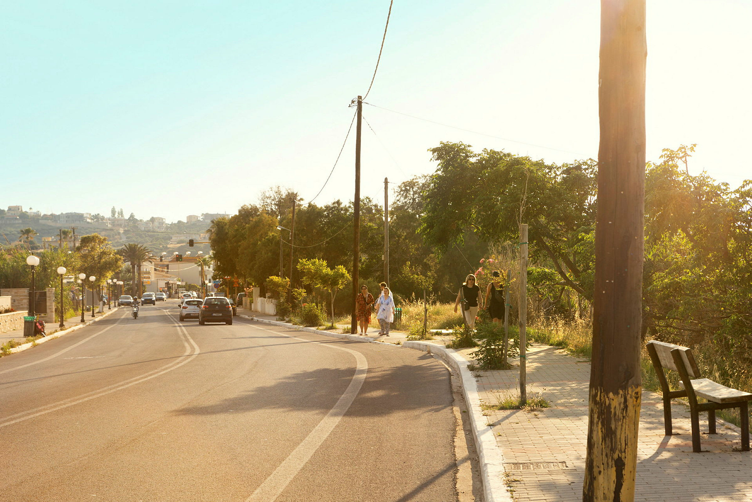 Aurinkoinen tie, jolla on pysäköityjä autoja ja jalankulkijoita jalkakäytävällä. (Tekoälyn luoma teksti)
