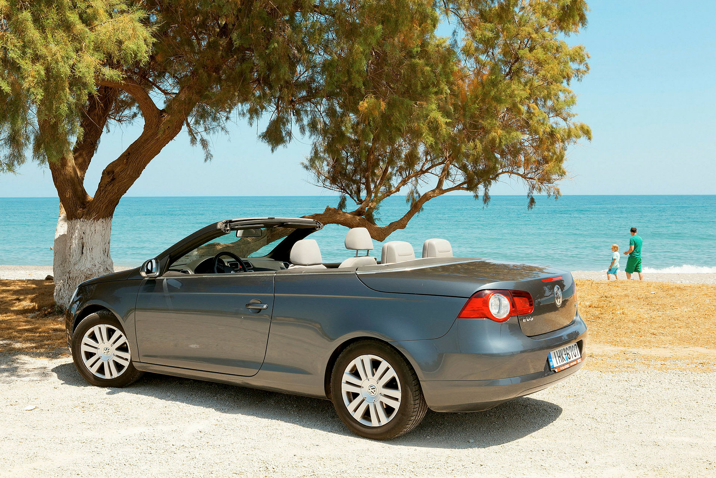 Harmaa cabriolet on pysäköity rannalle, taustalla meri ja puita. (Tekoälyn luoma teksti)