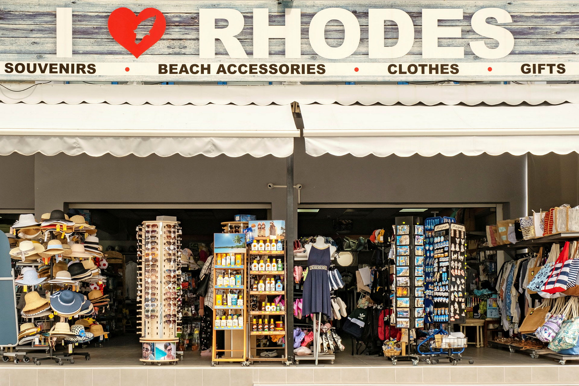 Kauppa, joka myy matkamuistoja ja rantatarvikkeita, kyltissä lukee "I ❤ RHODOS". (Tekoälyn luoma teksti)