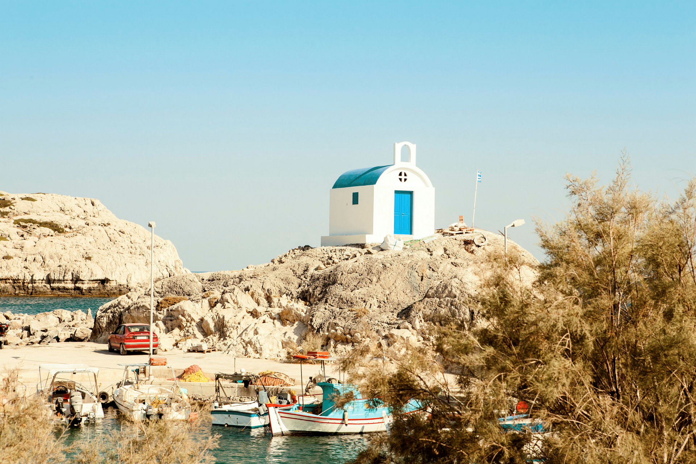 Valkoinen kirkko sinisellä katolla ja ovella kallion päällä veden ääressä ja pieniä kalastusveneitä. (Tekoälyn luoma teksti)