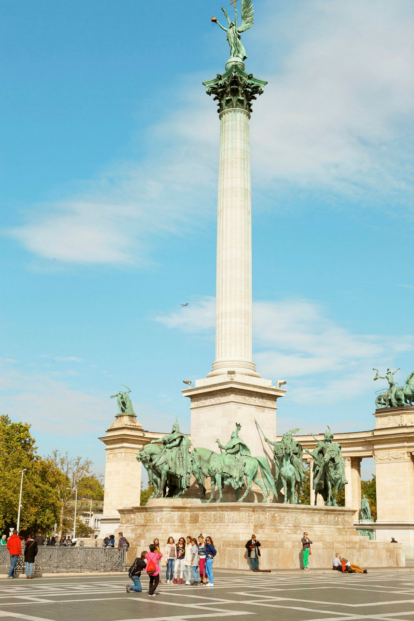 Korkea pylväs, jonka päällä on patsas, ympärillä on useita ratsupatsaita monumentilla avoimella aukiolla. (Tekoälyn luoma teksti)