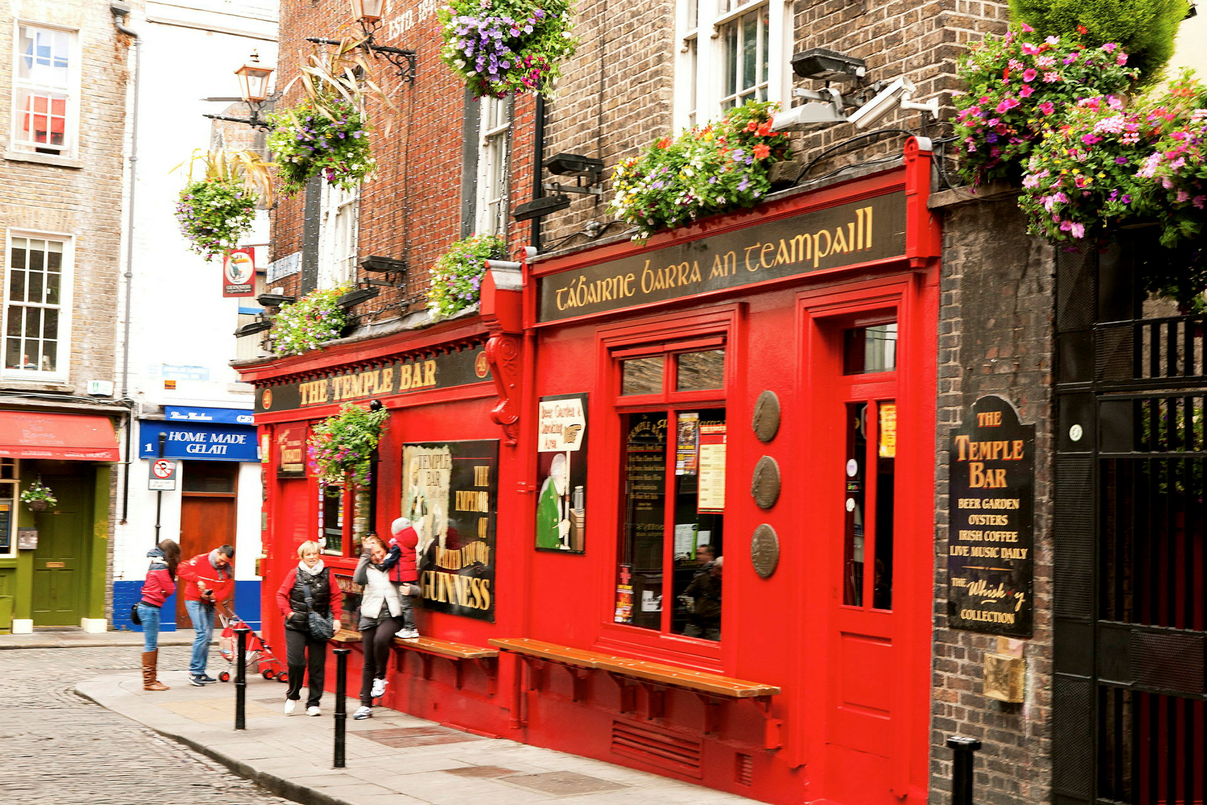 Punainen rakennus, jossa näkyy kyltti 'The Temple Bar', kukkalaatikoita ja ihmisiä ulkopuolella. (Tekoälyn luoma teksti)