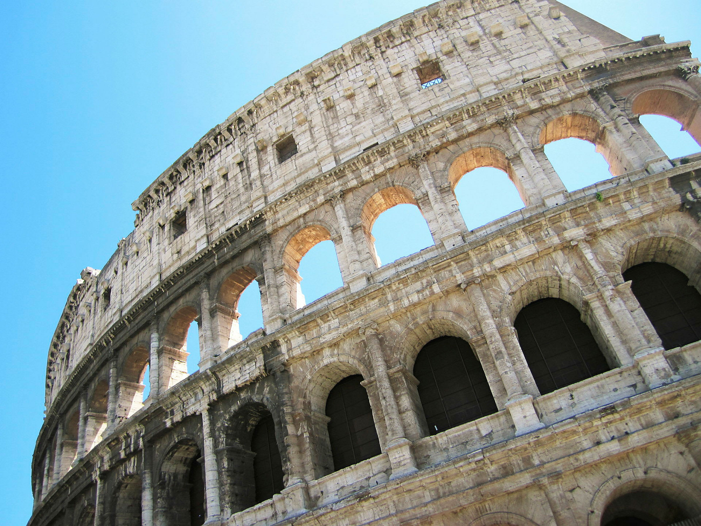 Valokuva Colosseumista Roomassa, Italiassa, kirkasta sinistä taivasta vasten. (Tekoälyn luoma teksti)
