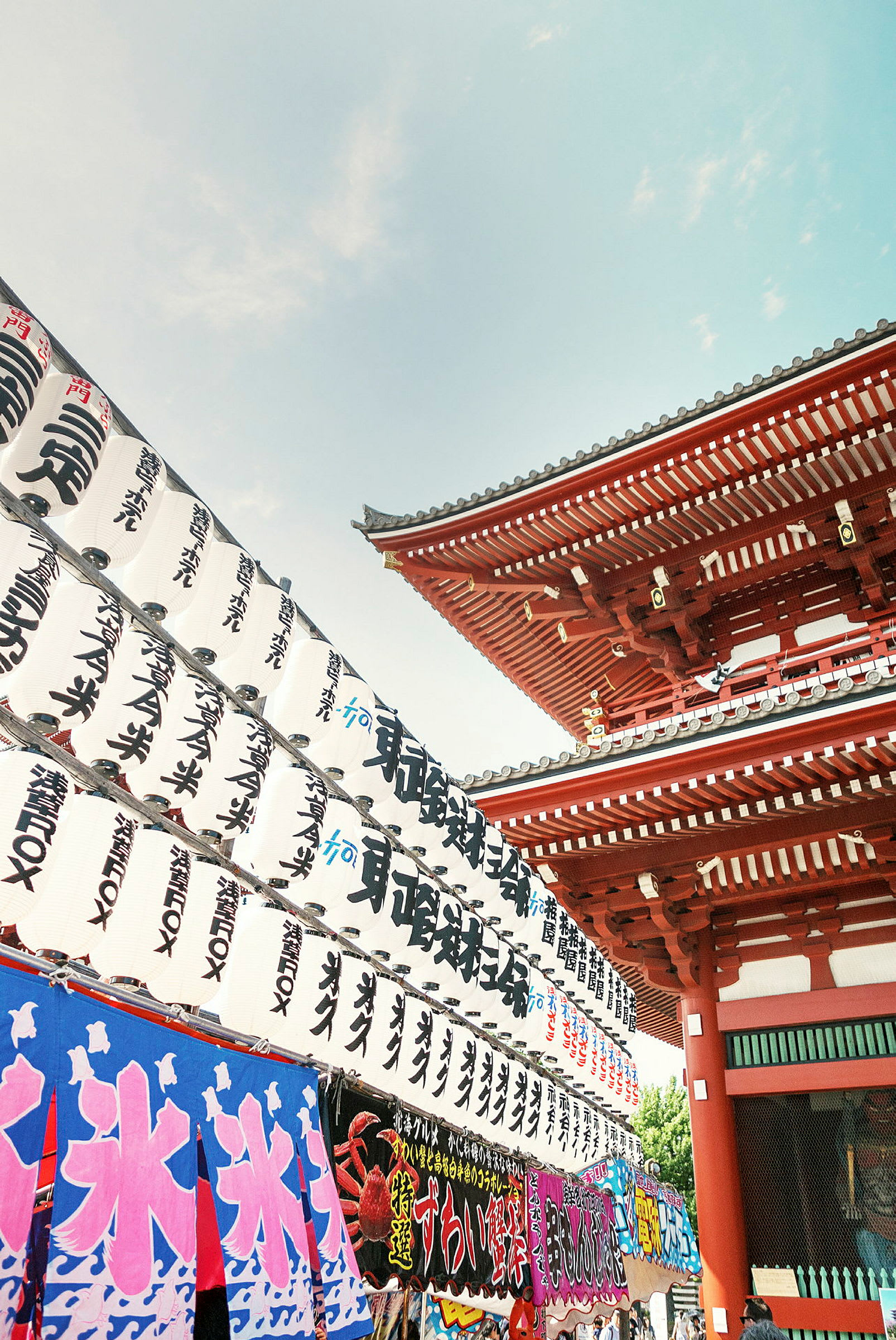 Japanilainen temppeli, jossa punaisia rakennuksia ja koristeita sekä perinteisiä valkoisia lyhtyjä japanilaisilla merkeillä. (Tekoälyn luoma teksti)