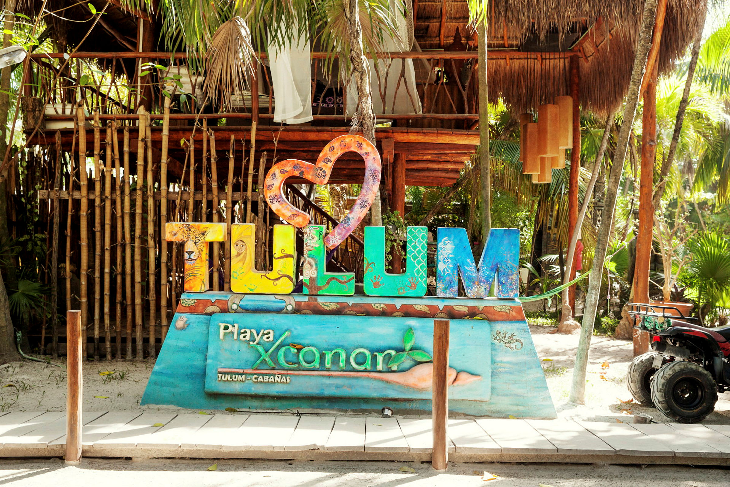 Värikäs Tulum-merkki tiheän metsän ja puurunkoisen rakennuksen edessä. (Tekoälyn luoma teksti)