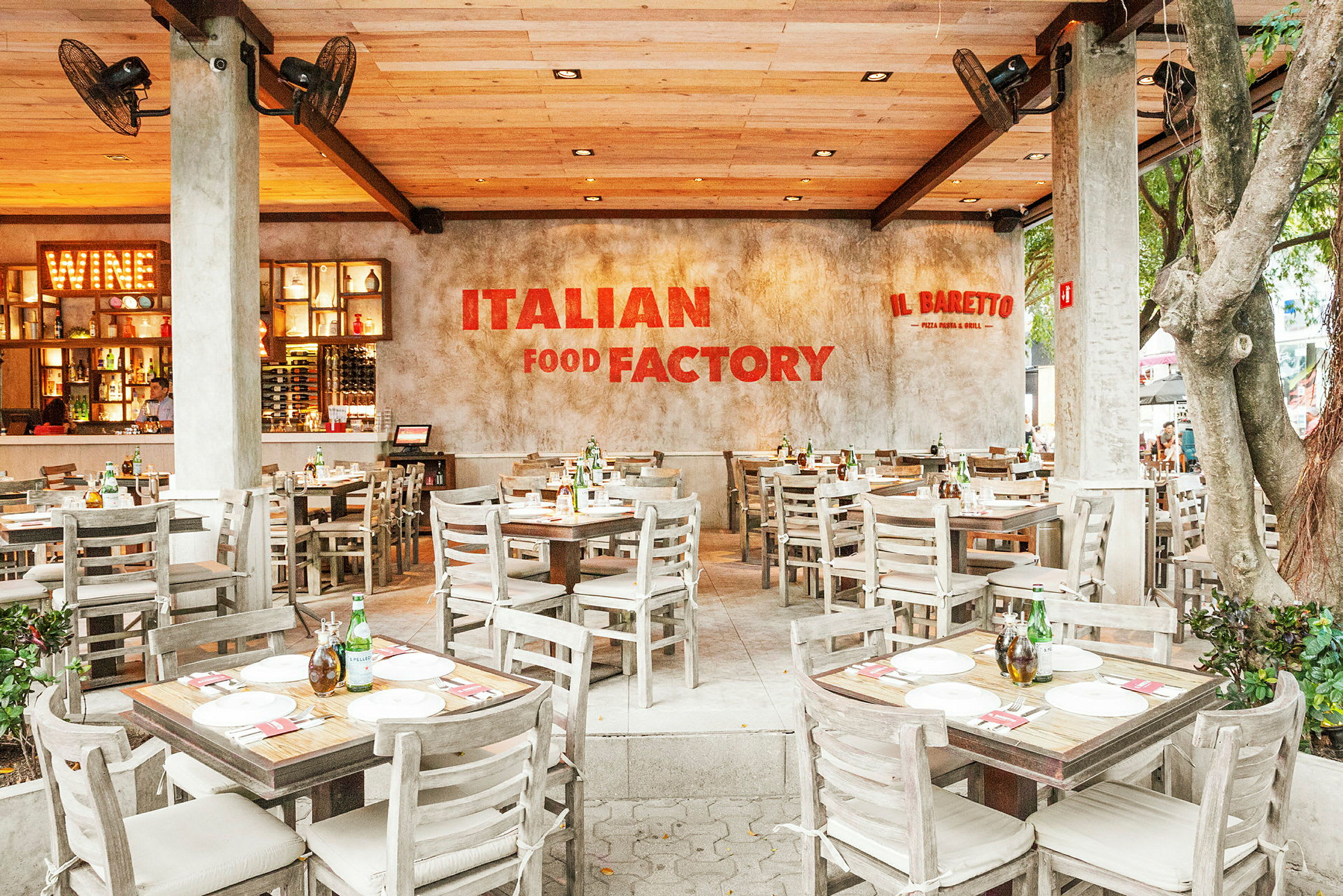 Italialainen ravintola, jossa on puiset pöydät ja tuolit, kutsuva tunnelma ja seinällä kyltti "Italian Food Factory". (Tekoälyn luoma teksti)