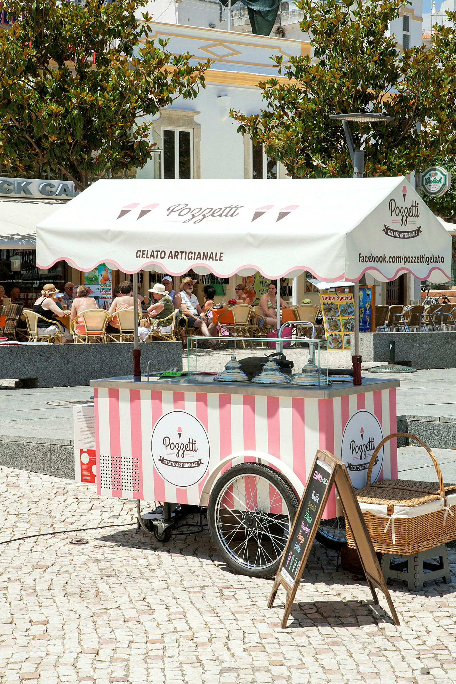 Liikkuva jäätelökioski, jossa on vaaleanpunaiset ja valkoiset raidat ja katos, jossa lukee 'Gelato Artigianale'. (Tekoälyn luoma teksti)