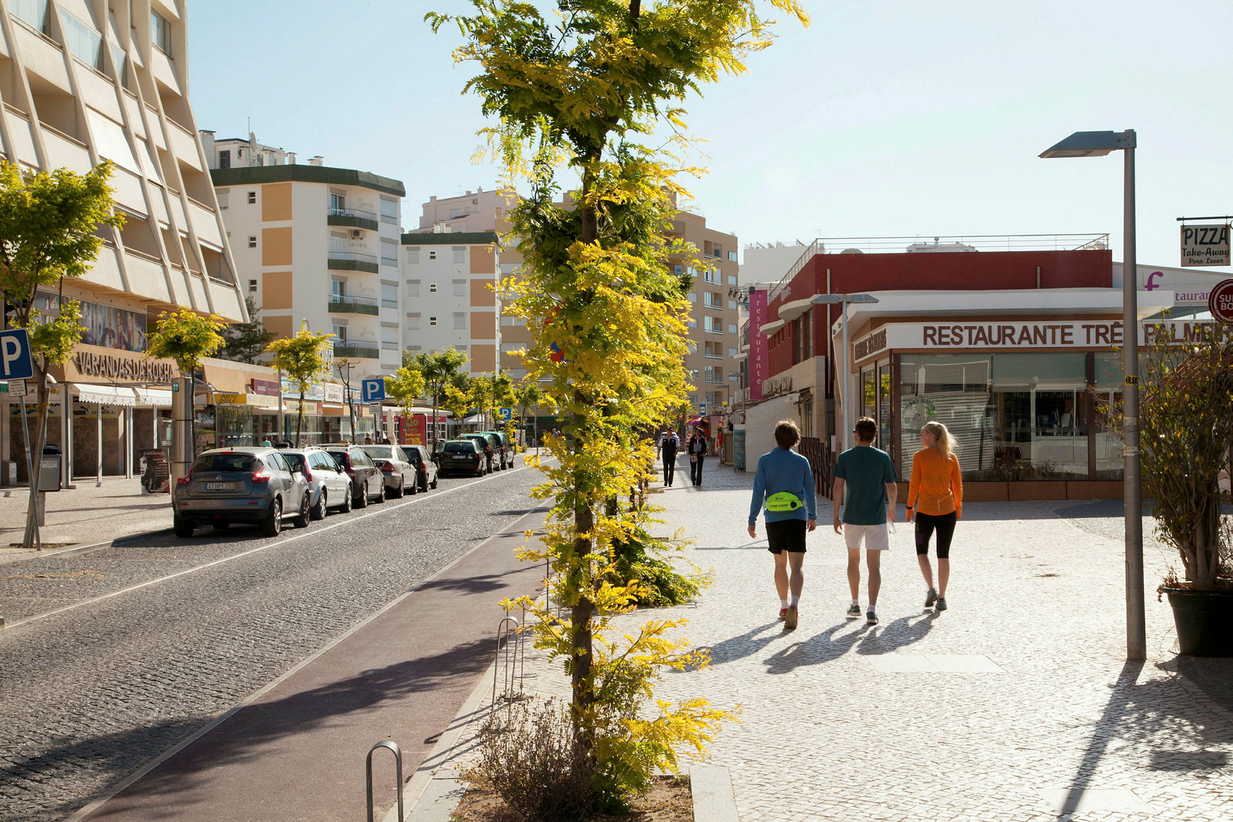 Ihmiset kävelevät kadulla, jonka varrella on pysäköityjä autoja ja rakennuksia taustalla. (Tekoälyn luoma teksti)