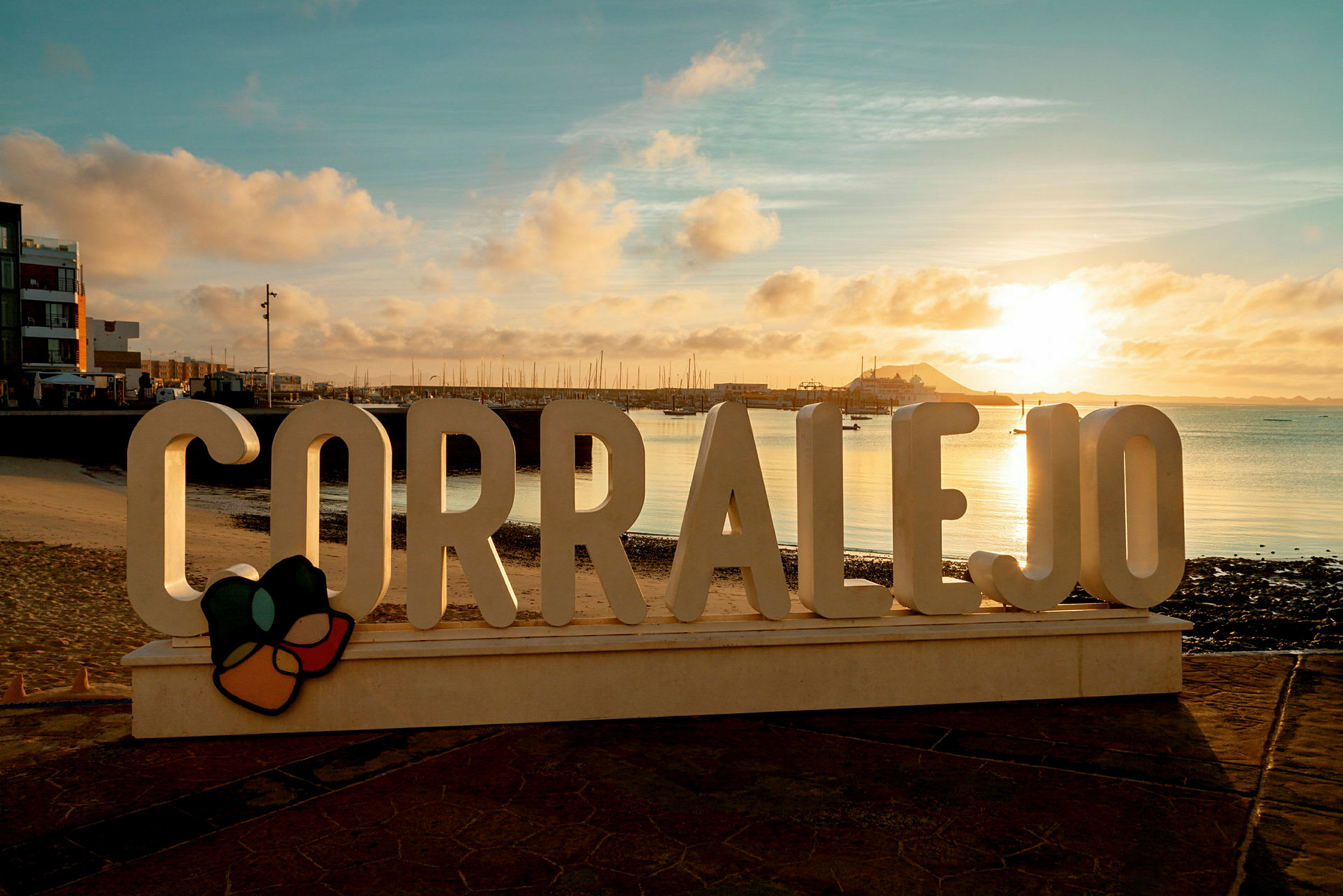 'Corralejo'-kyltti kävelytien varrella, taustalla meri ja laituri auringonlaskun aikana. (Tekoälyn luoma teksti)