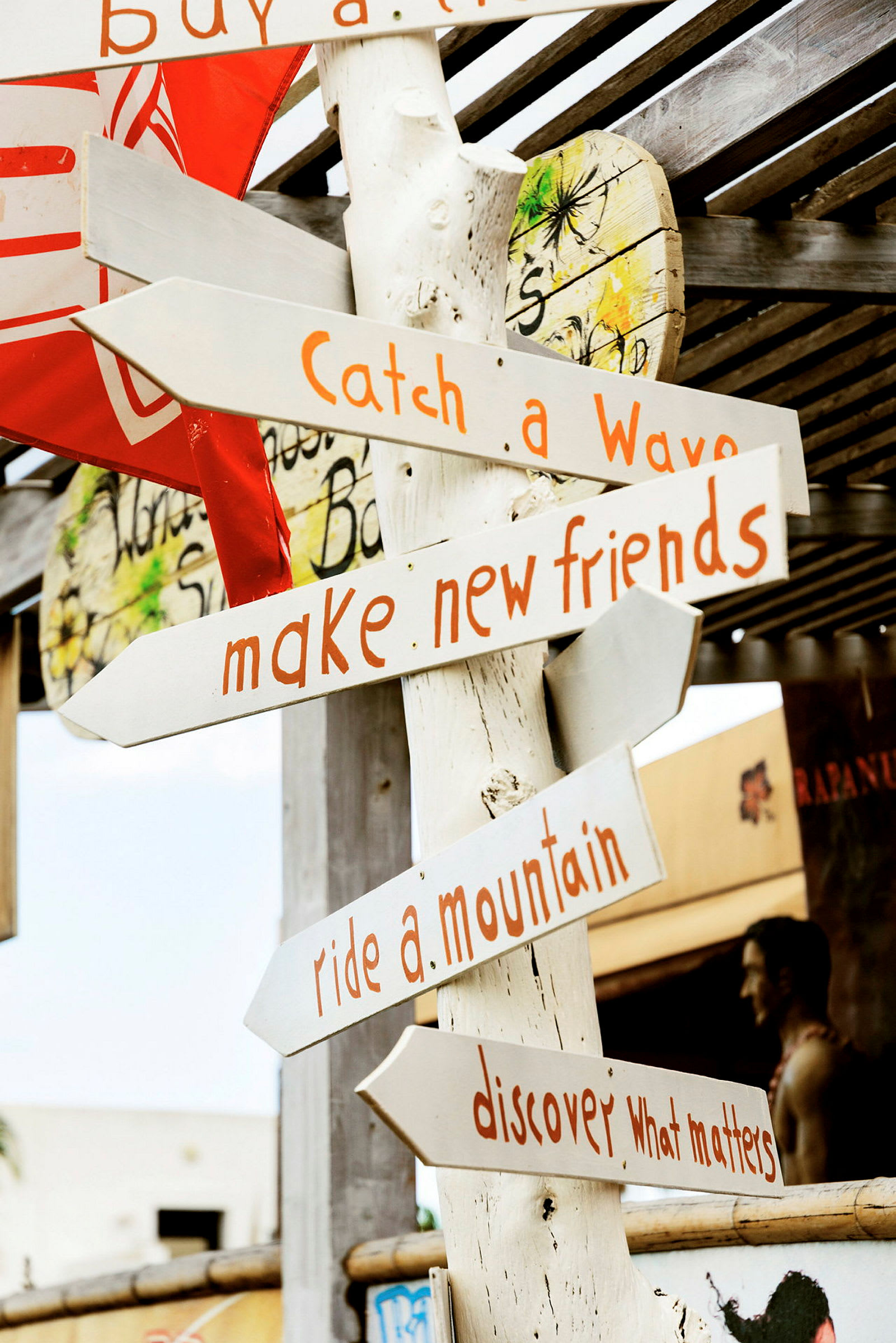 Puisessa opastaulussa on useita opasteita eri suuntiin ja tekstejä, kuten "Catch a Wave", "Make new friends", "Ride a mountain" ja "Discover what matters". (Tekoälyn luoma teksti)