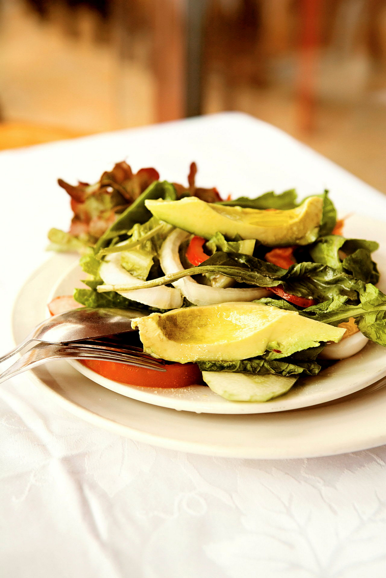 Salaatti, jossa on avocadoa, tomaattia, sipulia ja lehtivihanneksia, tarjoiltuna lautasella. (Tekoälyn luoma teksti)