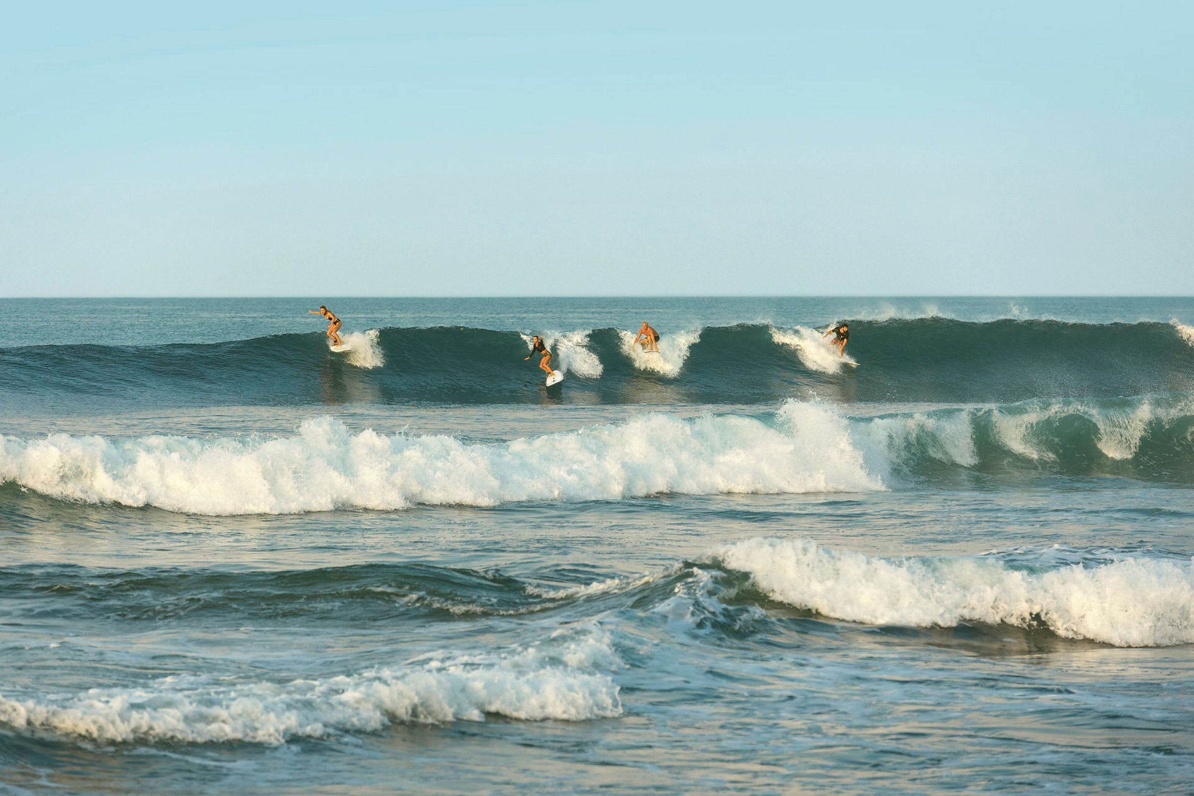 Neljä surffaajaa ratsastaa aalloilla meressä kirkkaan taivaan alla. (Tekoälyn luoma teksti)