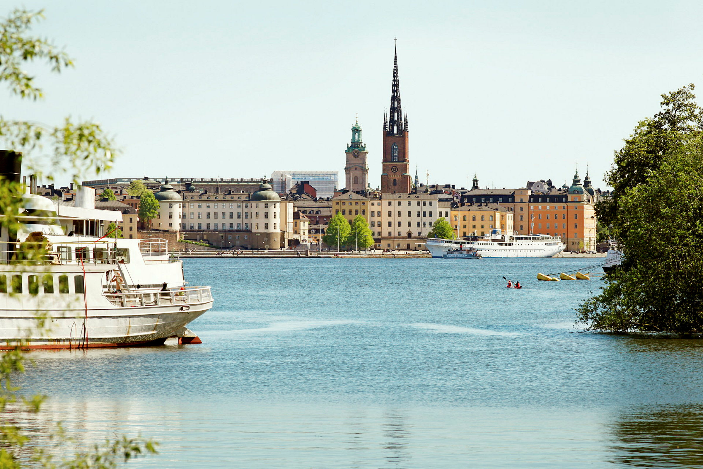 Kaupunkinäkymä, jossa rakennuksia, vettä ja kirkko, jossa on korkea torni, nähtynä veden ääreltä. (Tekoälyn luoma teksti)