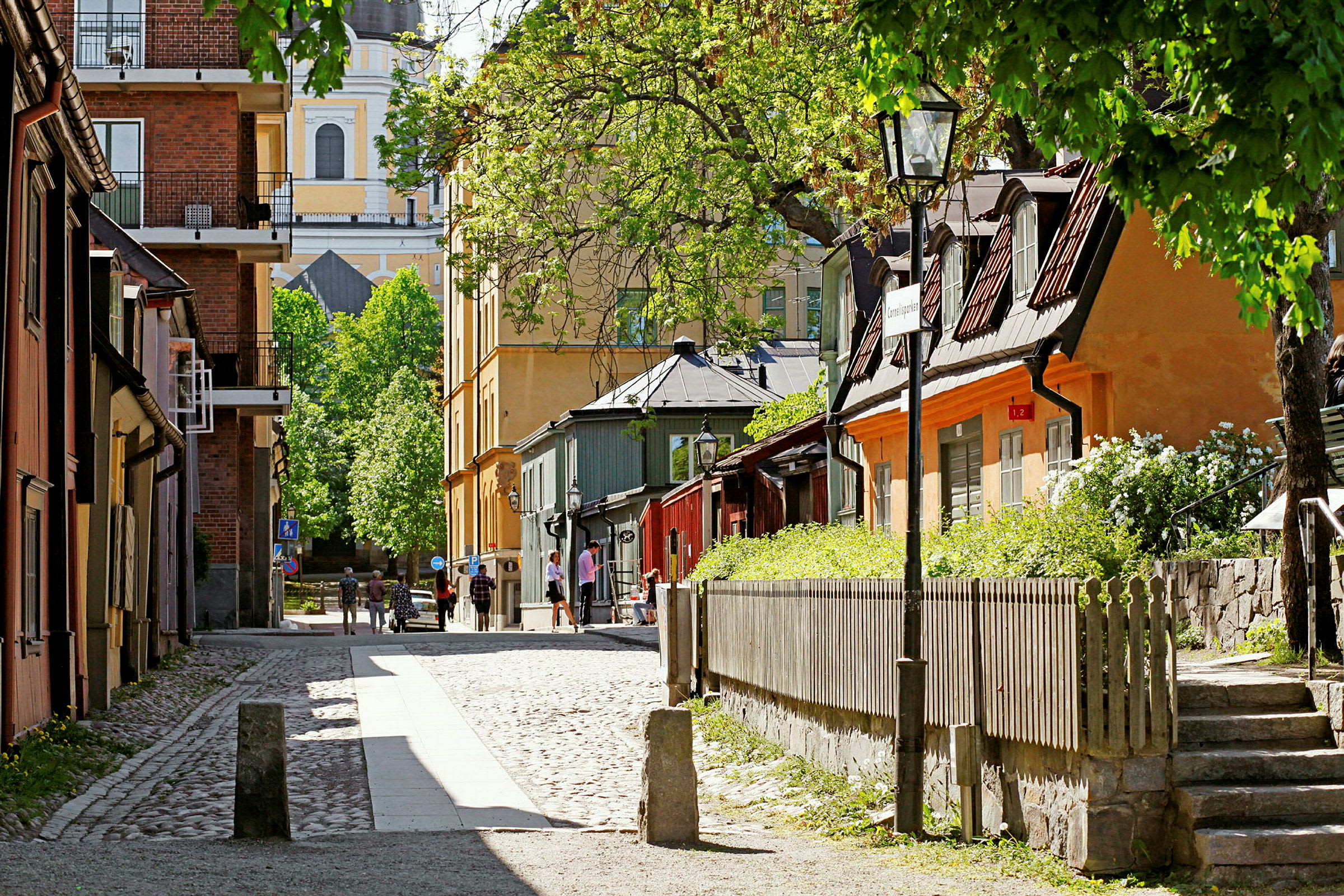 Kivipäällysteinen katu, jota reunustavat vanhat talot ja ympäröivät viheralueet ja puut. (Tekoälyn luoma teksti)