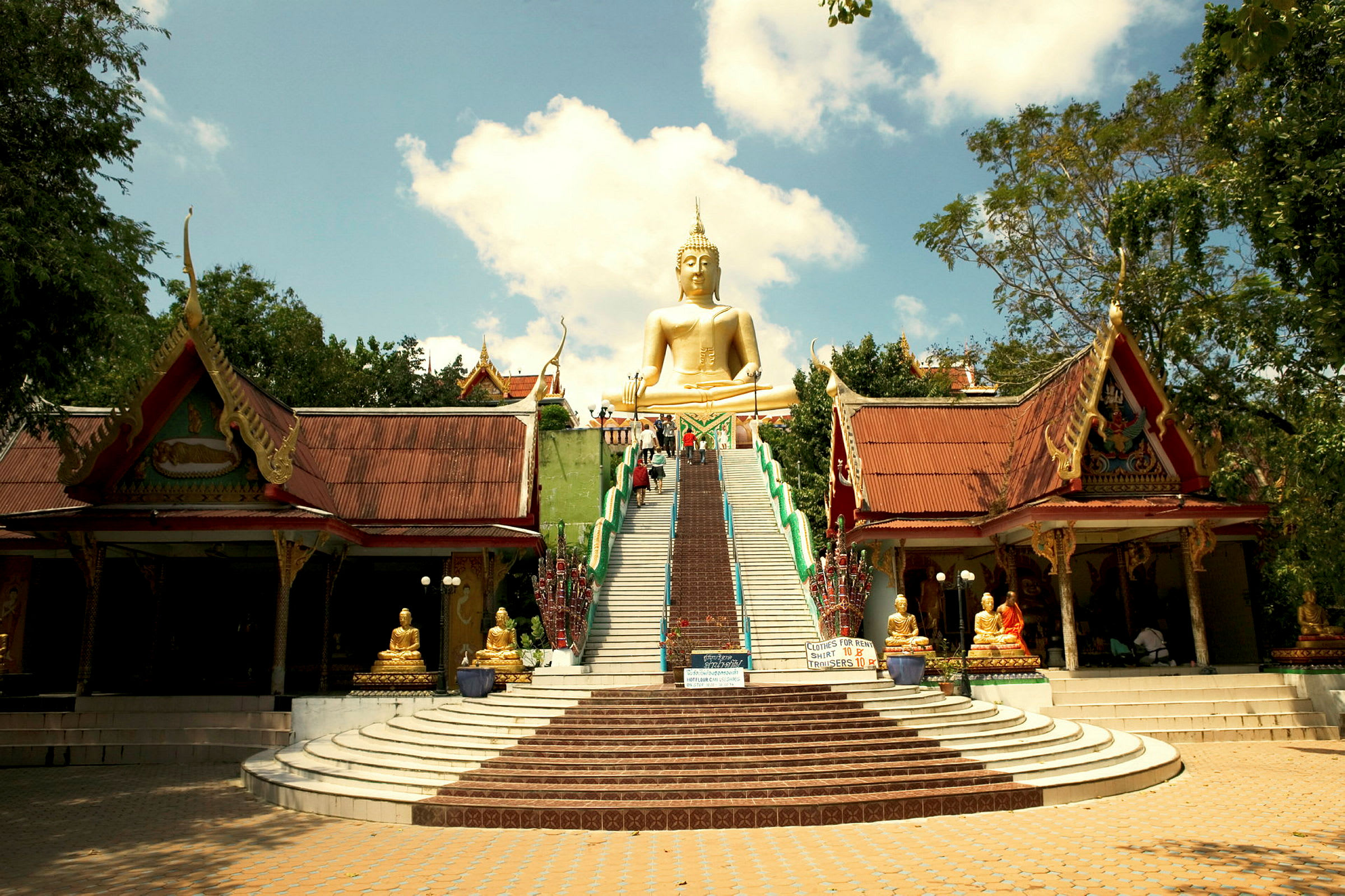 Suuri kultainen buddha portaikon huipulla, jossa on kaksi perinteistä rakennusta sivuilla. (Tekoälyn luoma teksti)