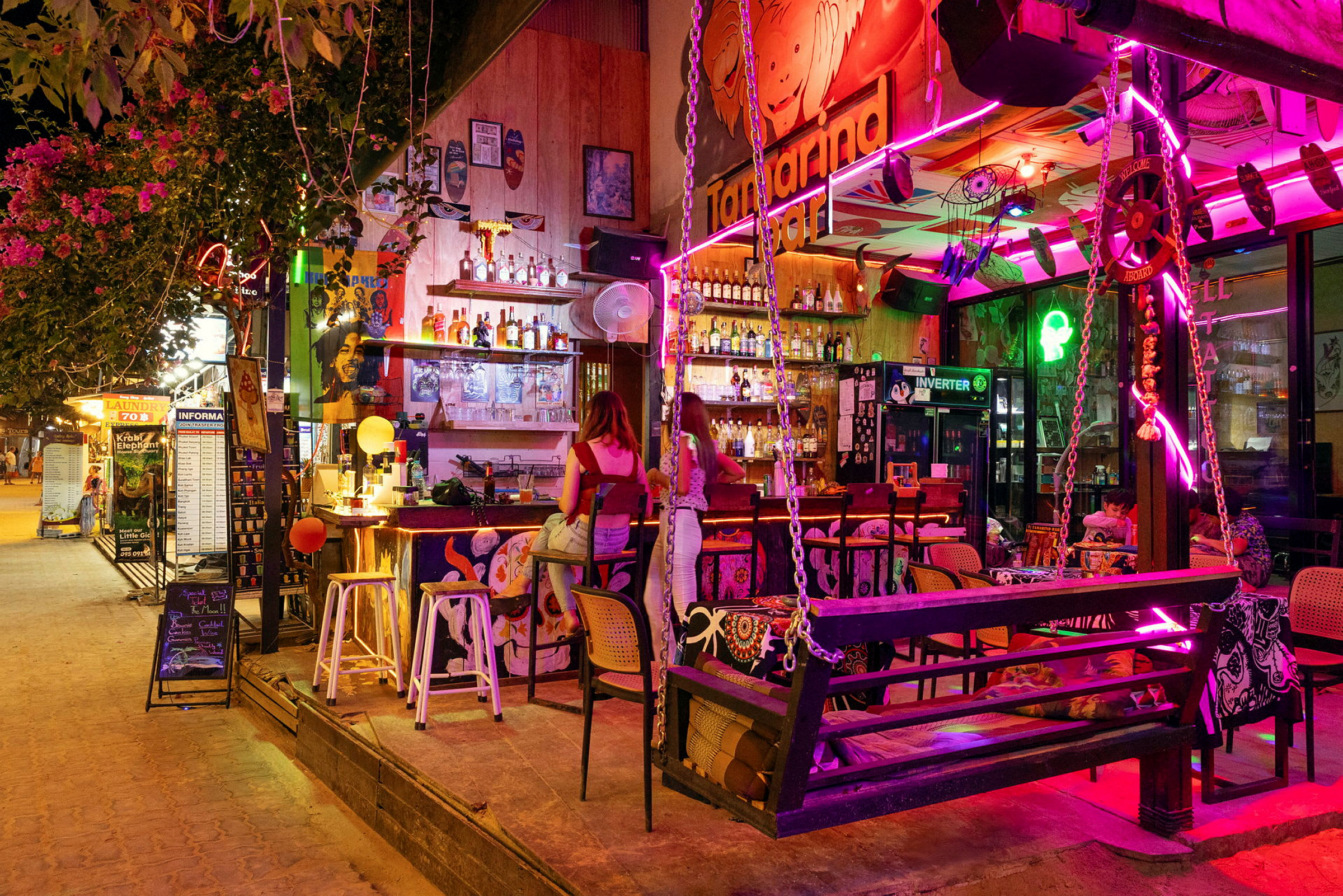Värikkäästi sisustettu baari kaupunkialueella, jossa on tuoleja ja pöytiä neonvalaistuksessa ja seinätaiteessa. (Tekoälyn luoma teksti)