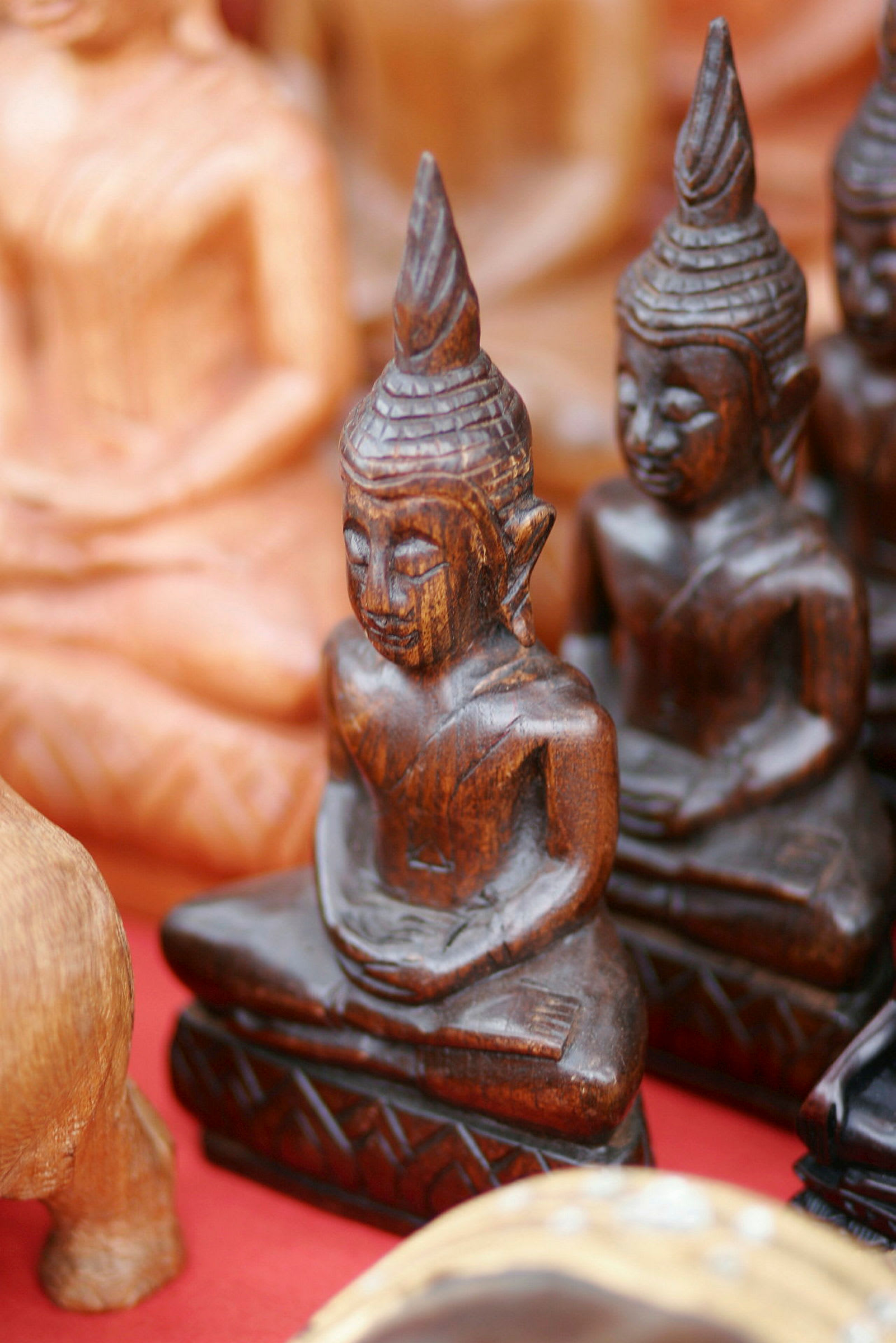 Kuva kokoelmasta pieniä, puisia Buddha-patsaita punaisella taustalla. (Tekoälyn luoma teksti)