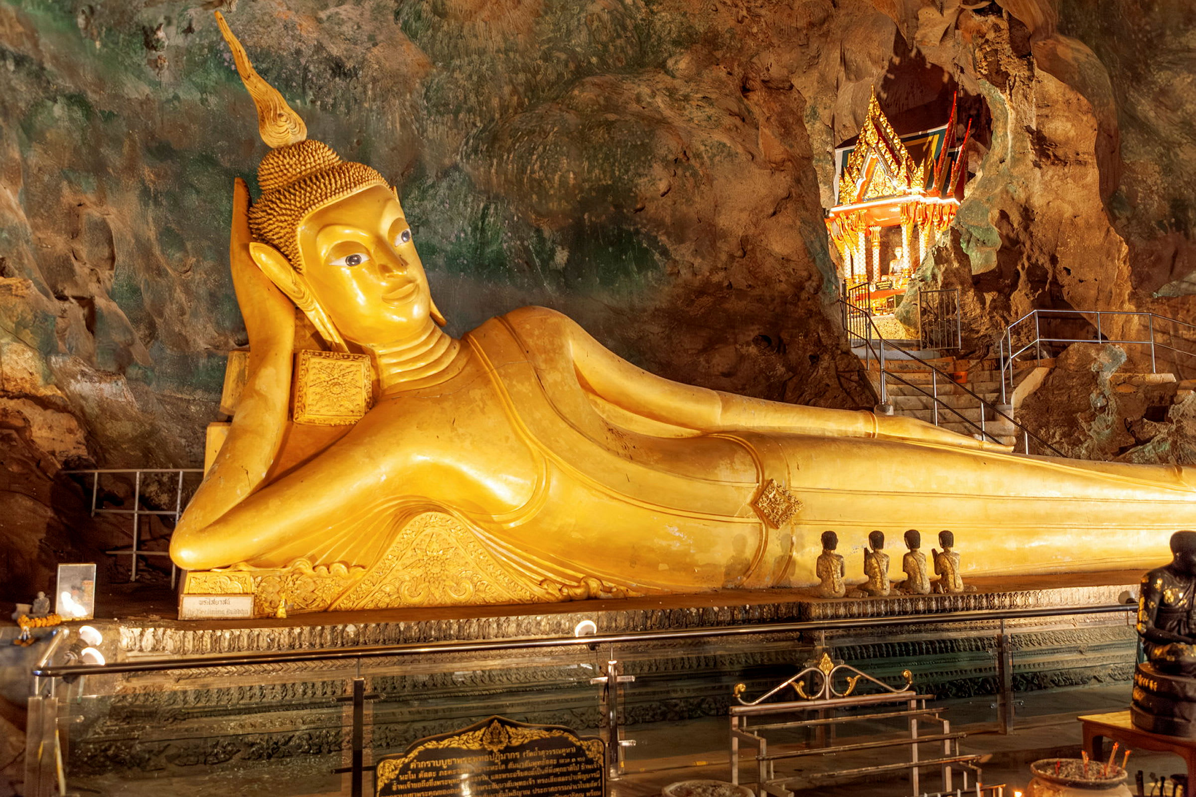 Kultainen makaava Buddha-patsas luolan sisällä, ympärillään kauniisti koristeltu alue yksityiskohtaisine koristeineen. (Tekoälyn luoma teksti)