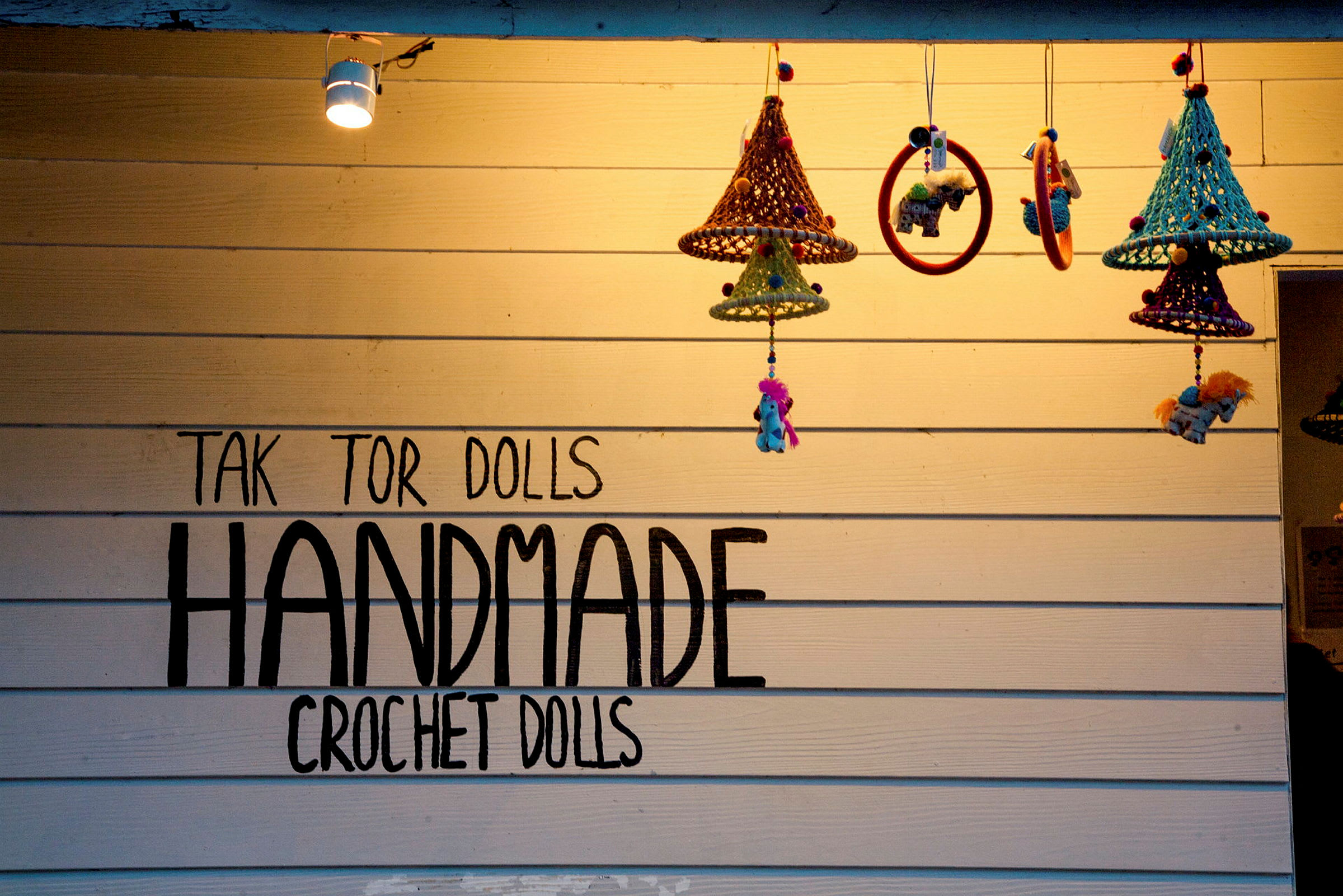 Seinä, jossa teksti 'Handmade Crochet Dolls' ja riippuvia virkattuja koristeita. (Tekoälyn luoma teksti)