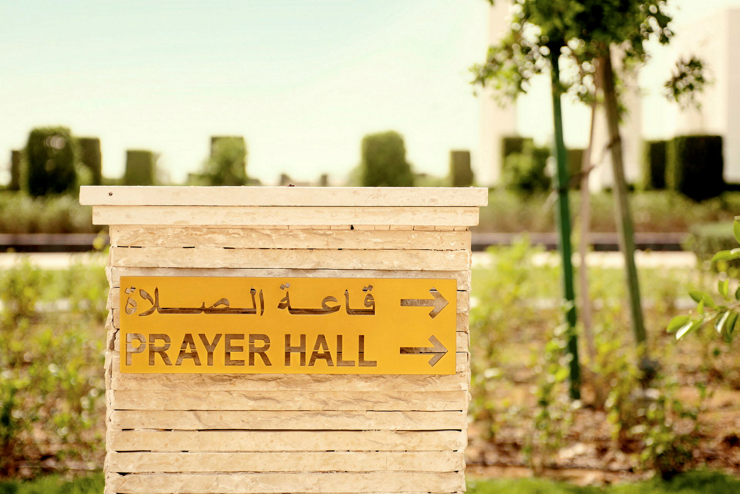 Kyltti, jossa lukee 'Prayer Hall' ja arabialainen teksti, osoittaa rukoushuoneeseen vehreyden keskellä. (Tekoälyn luoma teksti)