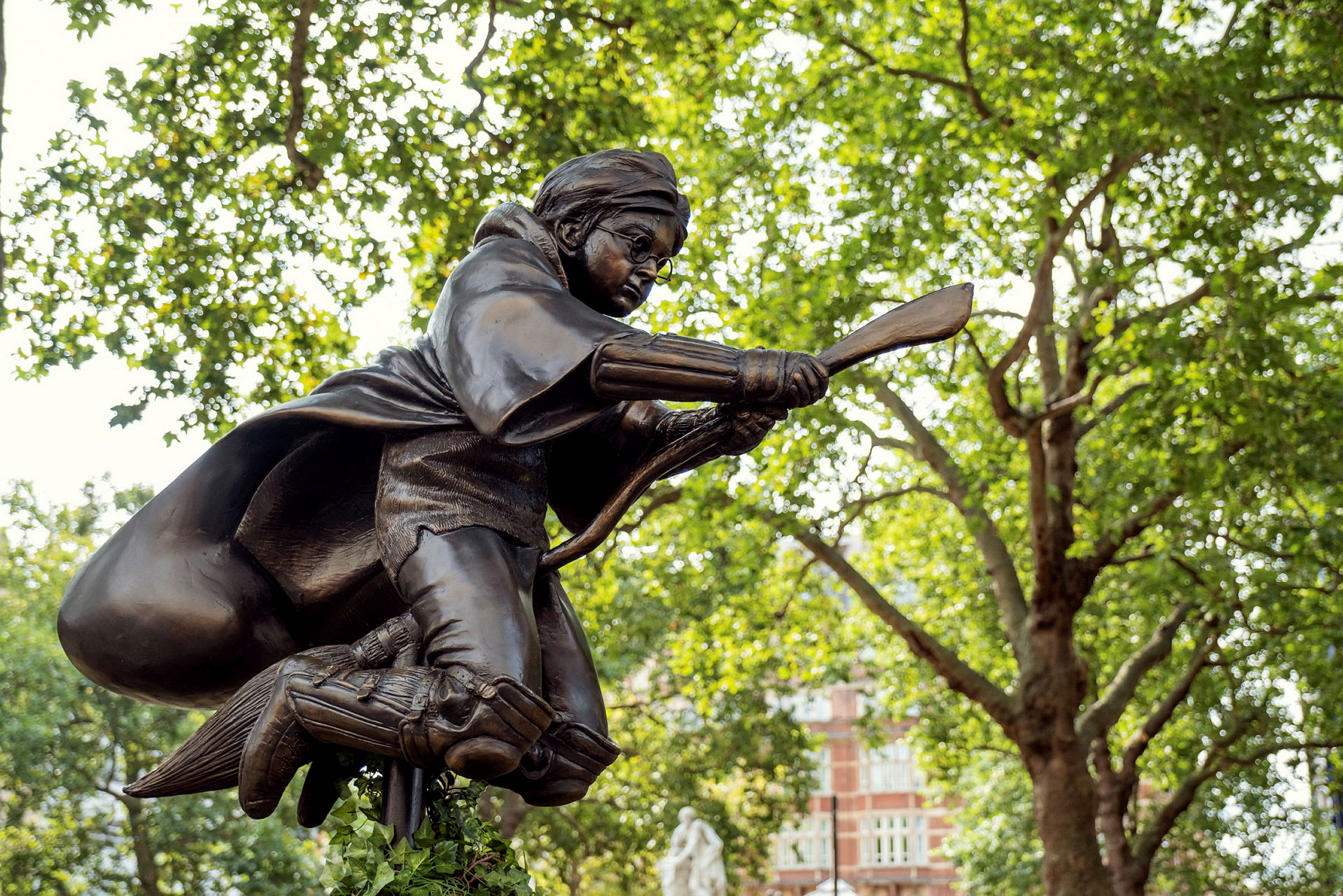 Patsas hahmosta, joka lentää luudan päällä, ympärillään puita ja rakennuksia. (Tekoälyn luoma teksti)