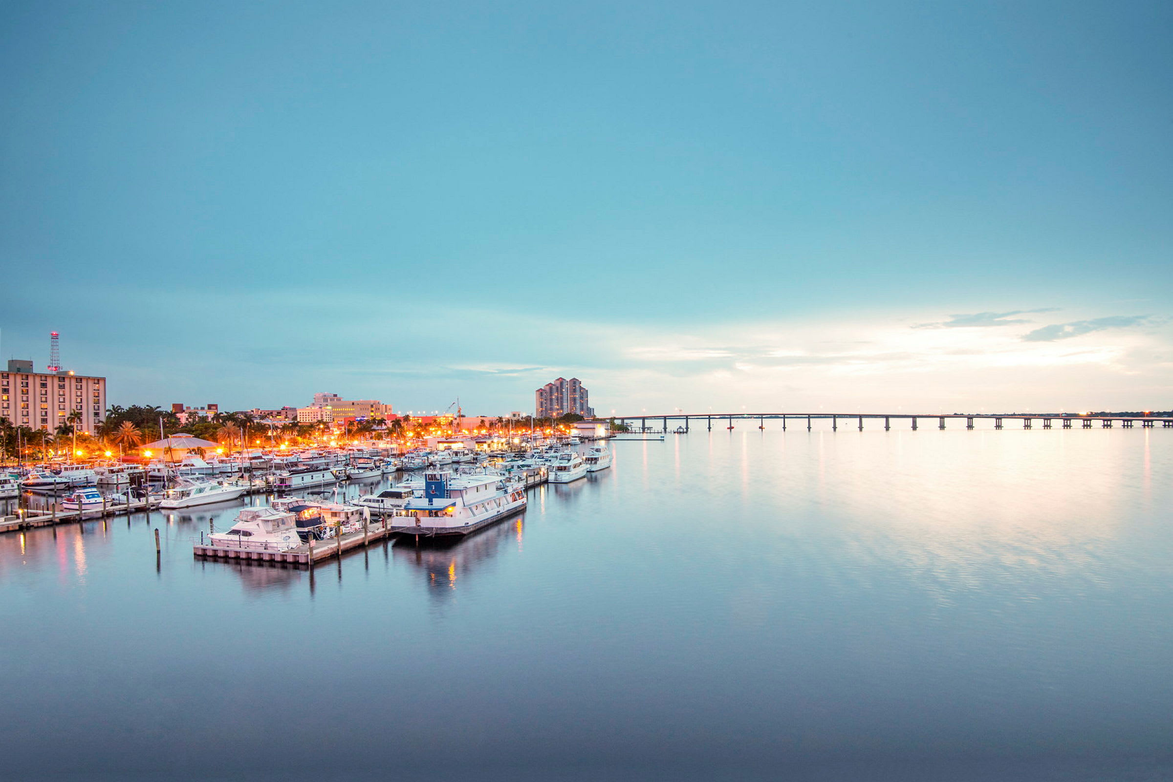 Venesatama, jossa on useita veneitä, kaupunki ja silta taustalla. (Tekoälyn luoma teksti)