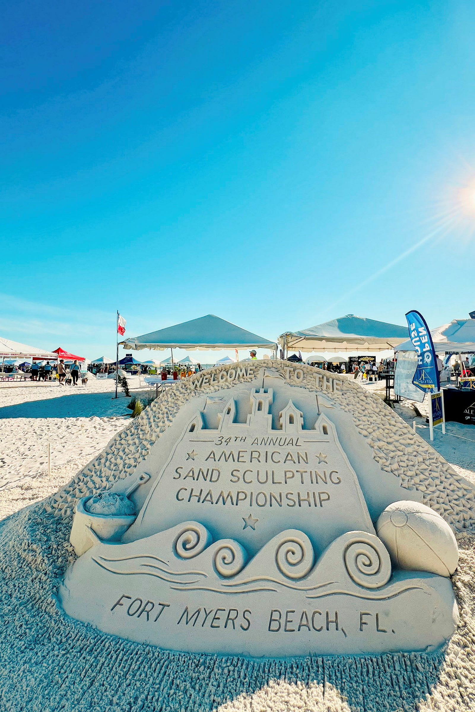 Hiekkapatsas tekstillä 'Fort Myers Beach, FL' ja 'American Sand Sculpting Championship'. (Tekoälyn luoma teksti)
