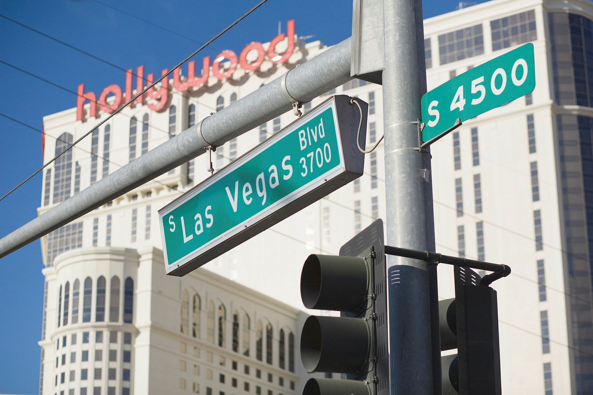 Kävelytien risteys, jossa liikennevalo ja katukyltit South Las Vegas Boulevardilla. Taustalla näkyy korkea rakennus ja teksti "hollywood". (Tekoälyn luoma teksti)