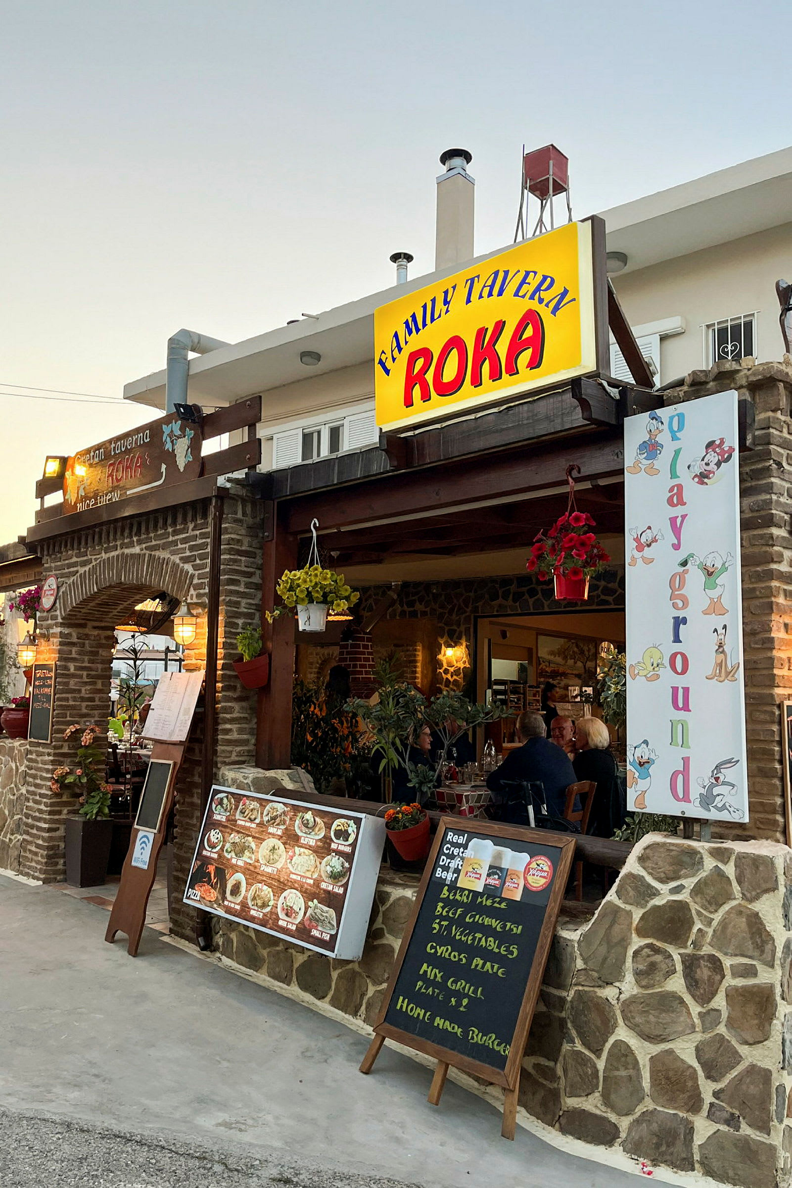 Ravintola, jossa kylttejä, ruokalistoja ja koristeita sisäänkäynnin luona. Sisällä näkyy pöytiä ja tuoleja. (Tekoälyn luoma teksti)