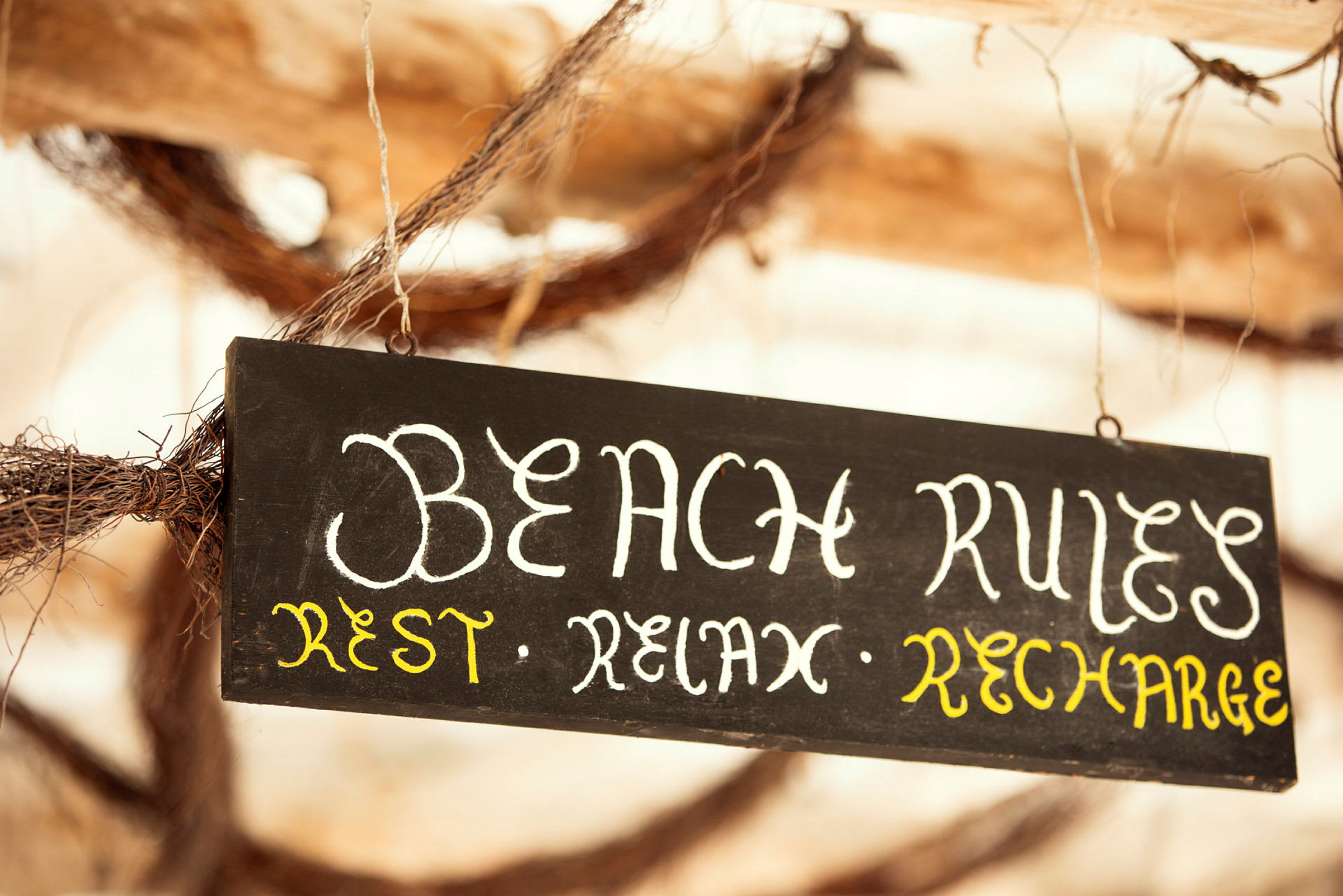 Musta kyltti tekstillä 'Beach Rules: Rest, Relax, Recharge'. (Tekoälyn luoma teksti)