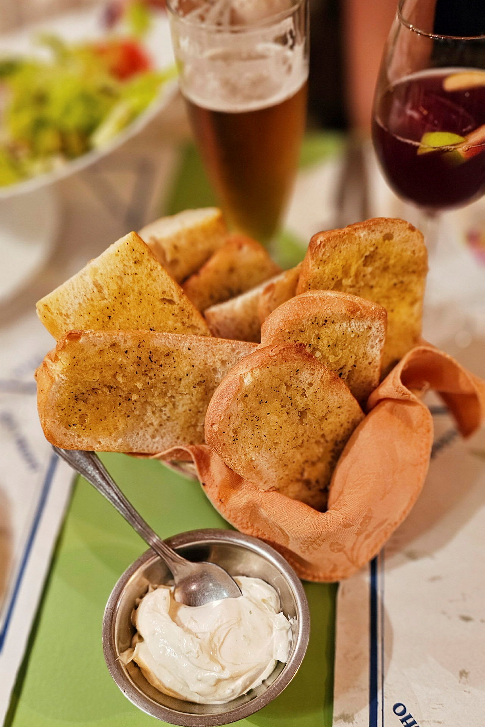 Valkosipulileipää tarjoiltuna kulhollisen dipin kanssa, taustalla lasit olutta ja sangriaa. (Tekoälyn luoma teksti)
