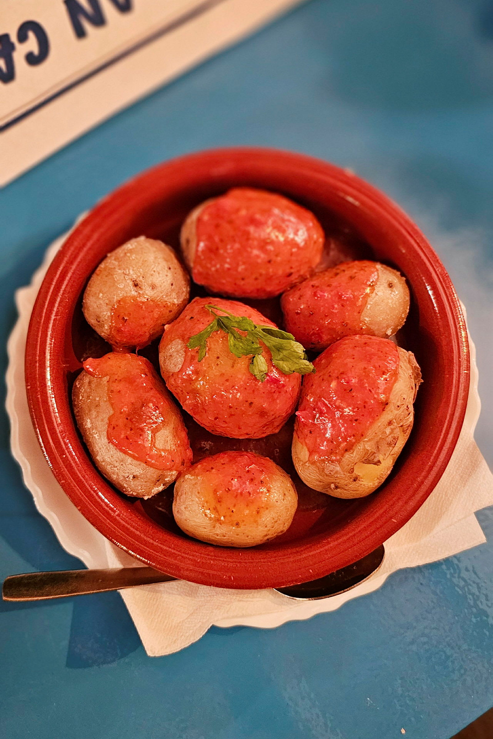 Kulhossa pieniä perunoita punaisella kastikkeella, koristeltu vihreällä lehdellä. (Tekoälyn luoma teksti)