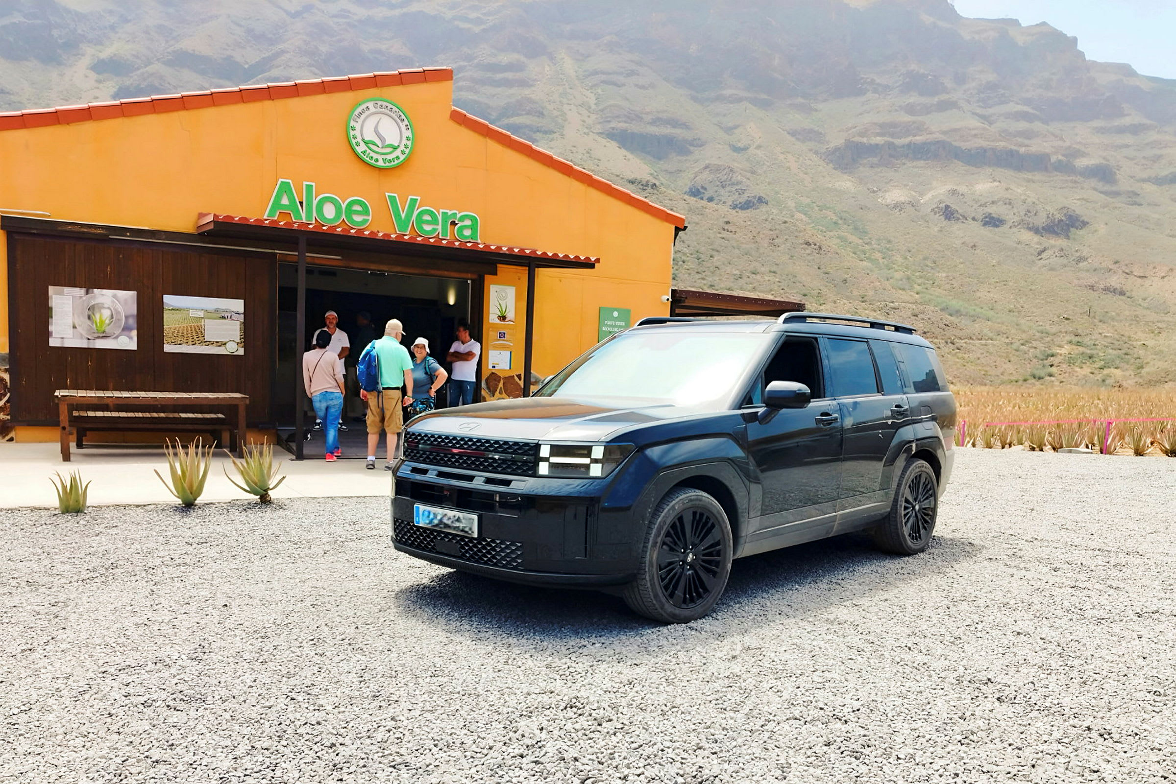 Musta SUV-pakettiauto on pysäköity rakennuksen eteen, jossa on kyltti 'Aloe Vera'. (Tekoälyn luoma teksti)