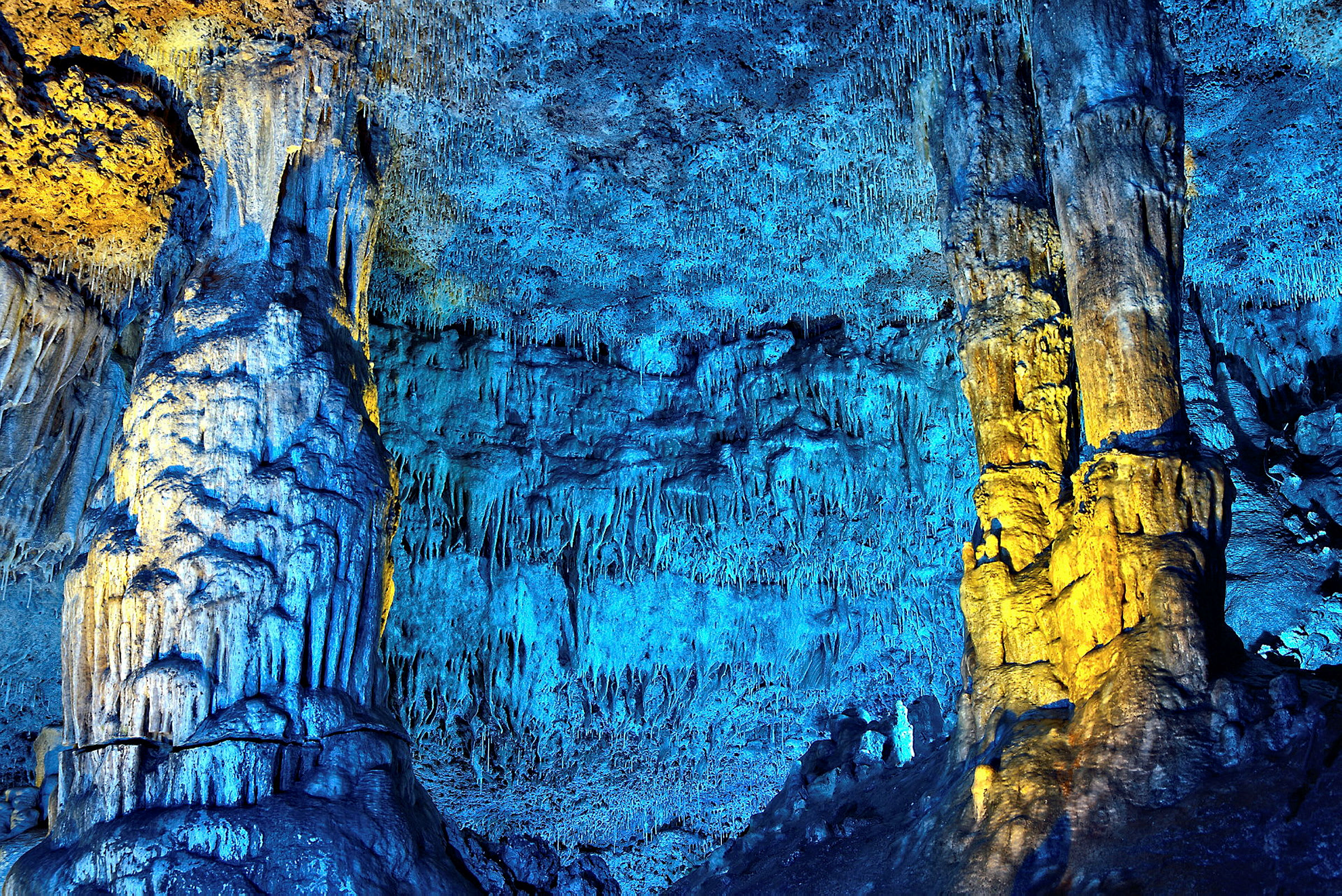 Tippukiviluola, jossa on värikästä valaistusta, joka valaisee stalaktiitteja ja stalagmiitteja. (Tekoälyn luoma teksti)