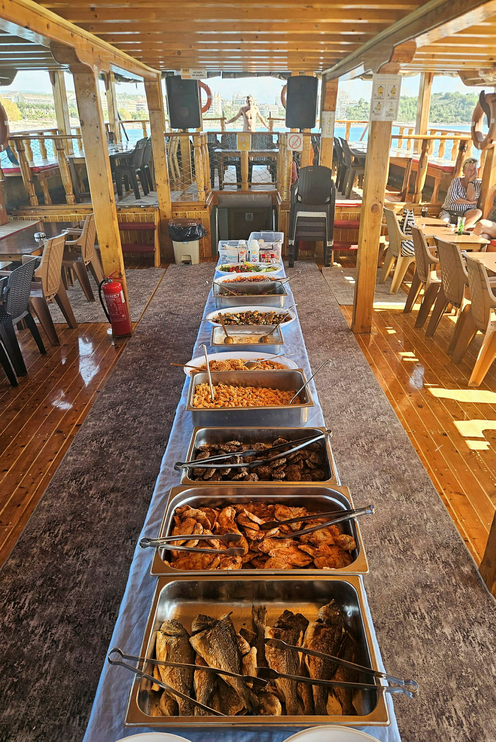 Buffet, jossa on erilaisia ruokia, on asetettu pitkälle riville katetulle laivan kannelle. (Tekoälyn luoma teksti)